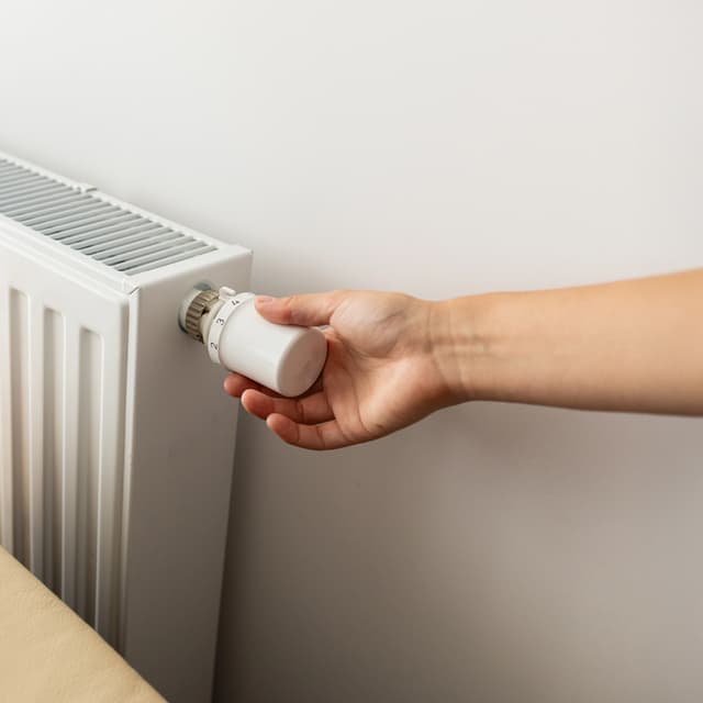 Hand dreht das Thermostat an einem klassischen Heizkörper auf