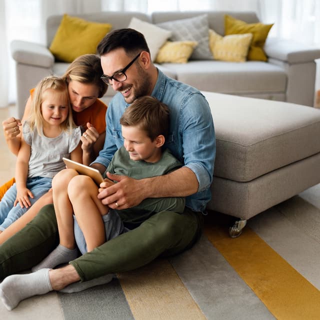 Glückliche Familie sitzt im Wohnzimmer auf dem Boden und schaut zusammen auf ein Tablet
