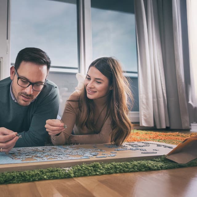 Paar liegt auf dem Boden und puzzelt gemeinsam in gemütlicher Wohnumgebung