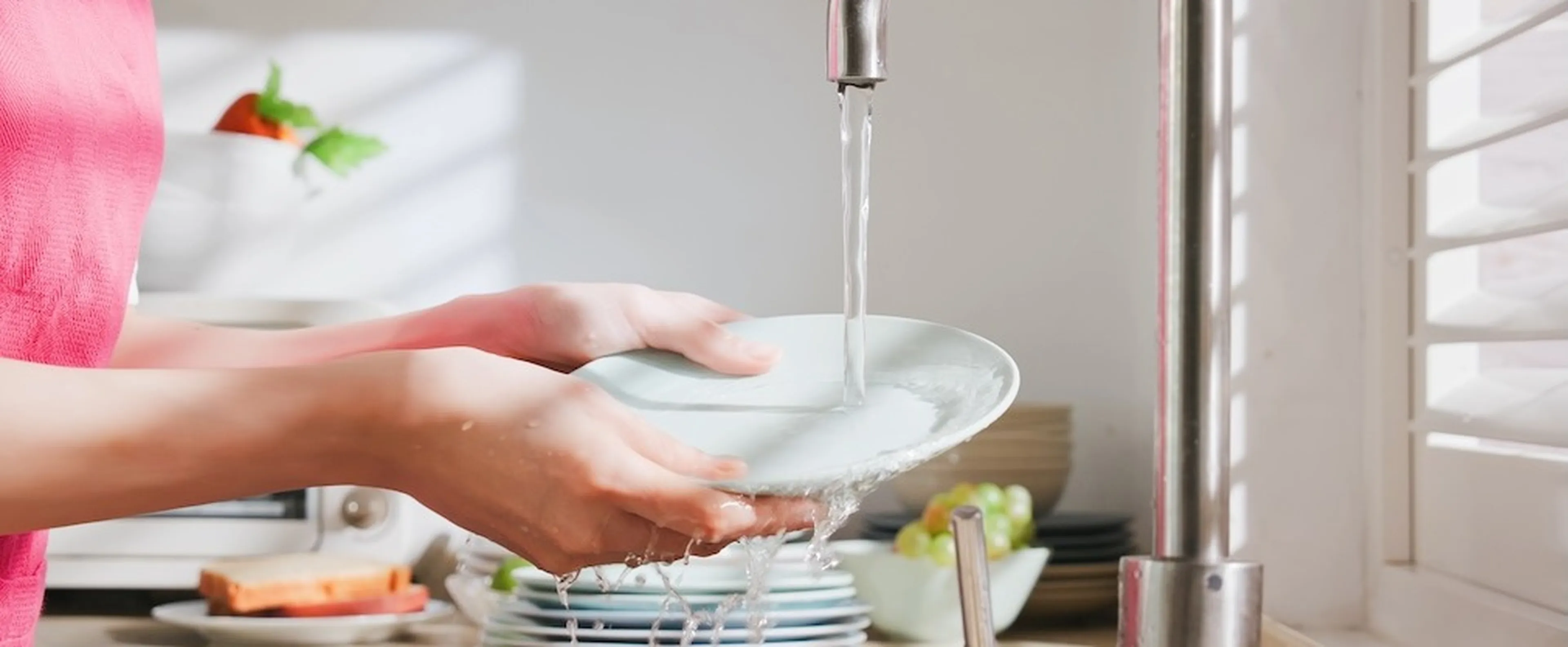 Frau spült einen weißen Teller unter dem Wasserhahn.