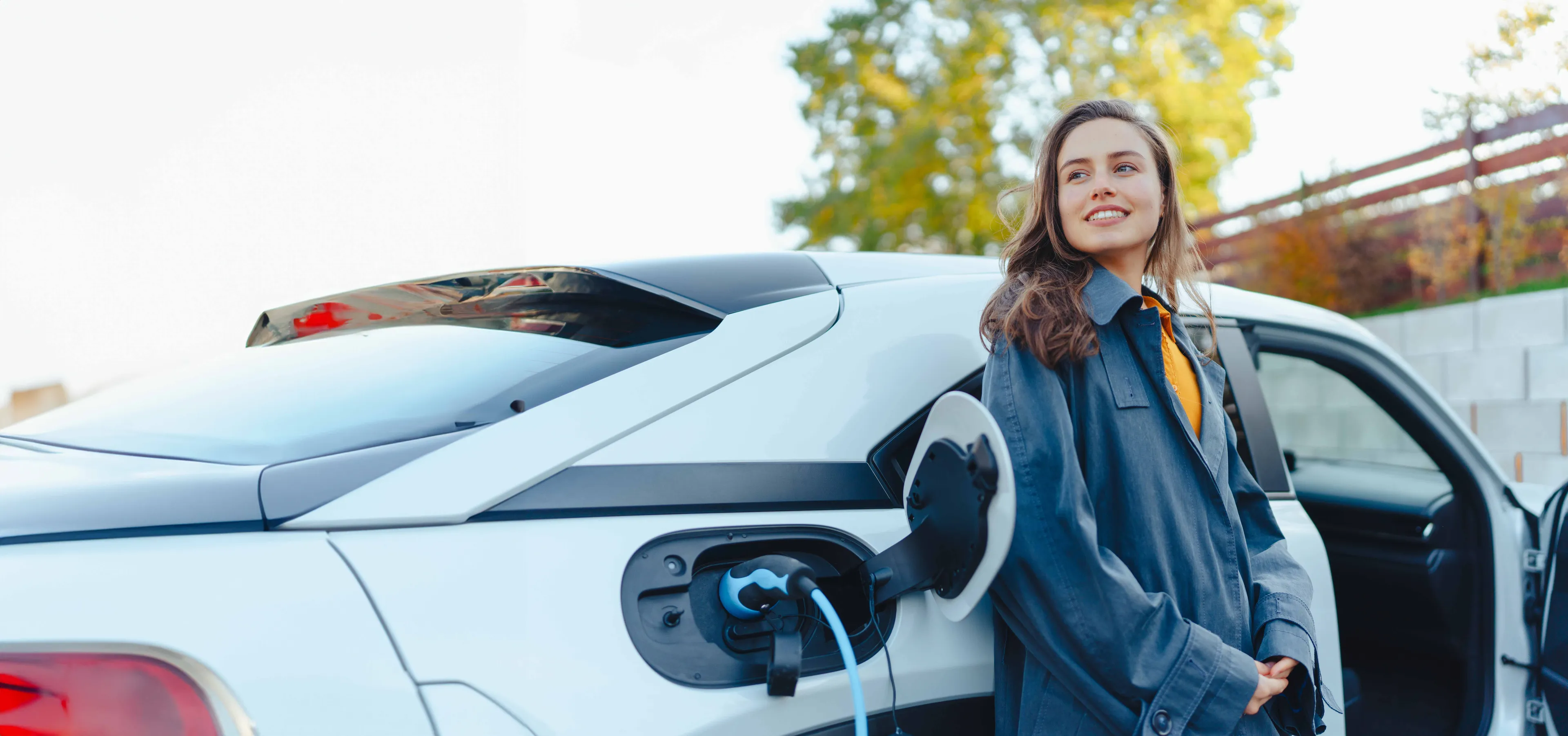 Frau lehnt lächelnd an weißem Elektroauto, das gerade geladen wird