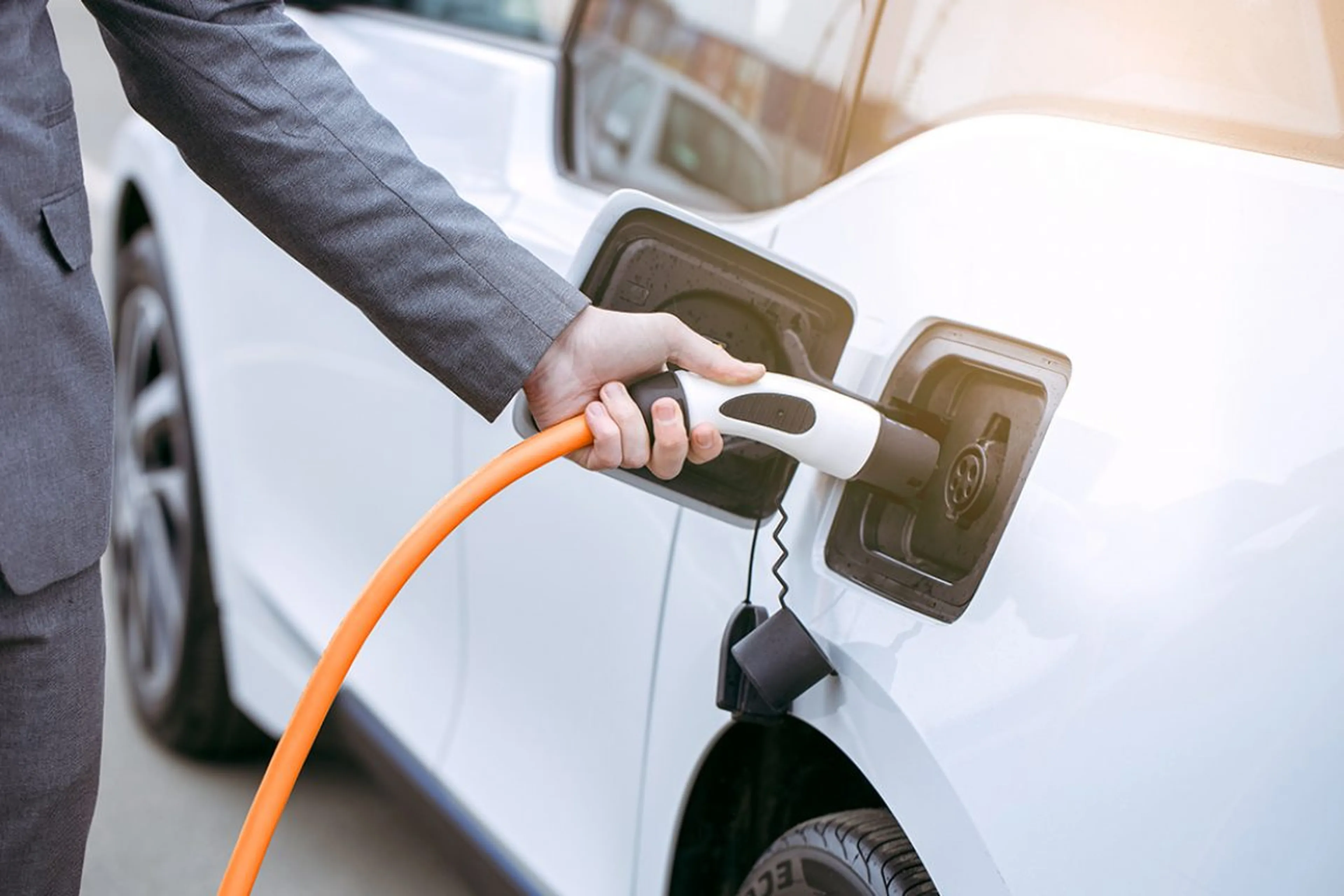 Person in Businesskleidung schließt ein Elektroauto mit einem orangefarbenen Ladekabel an eine Ladestation an