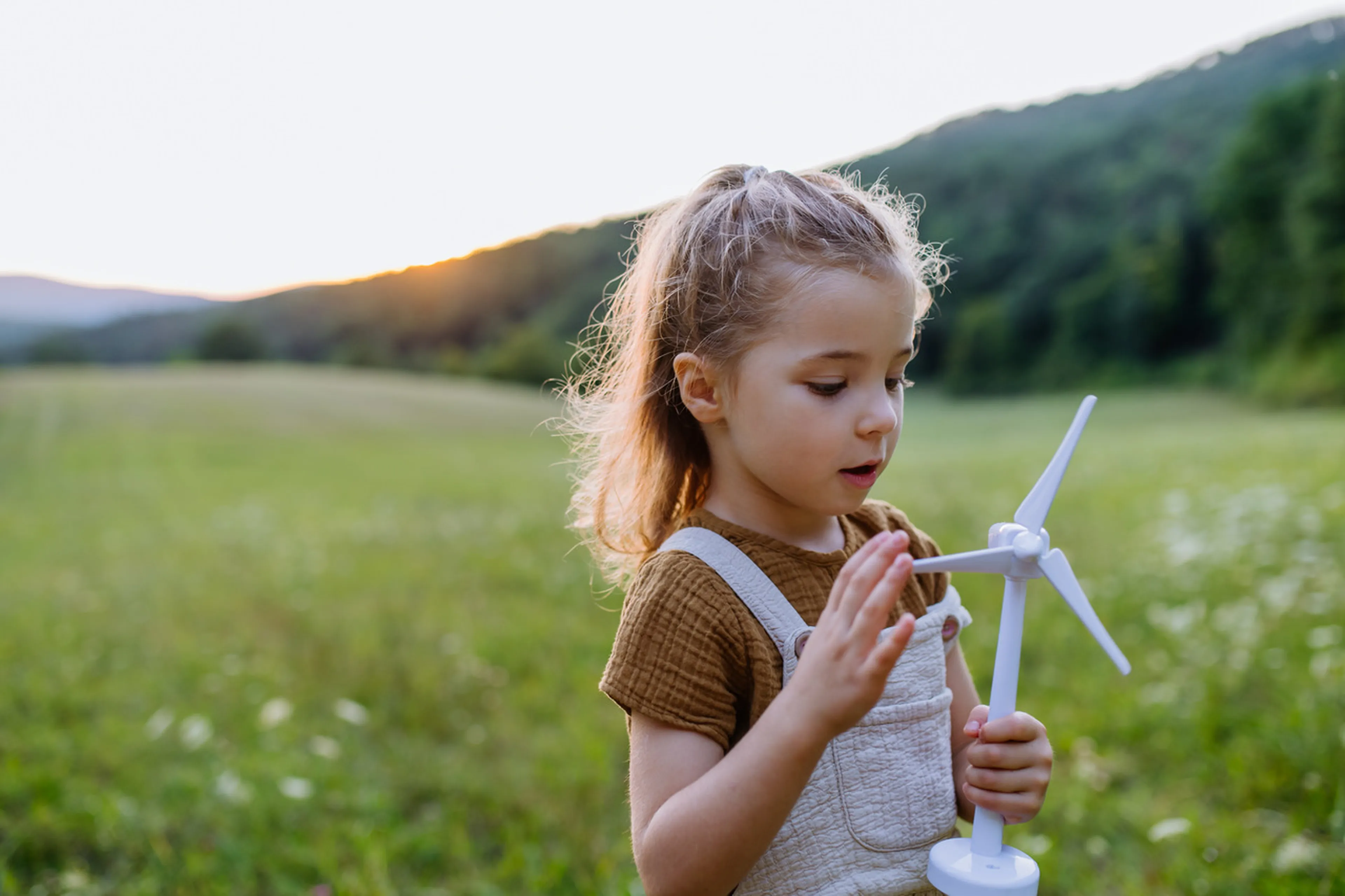 Kind steht auf Feld mit Mini-Windkraftanlage in der Hand