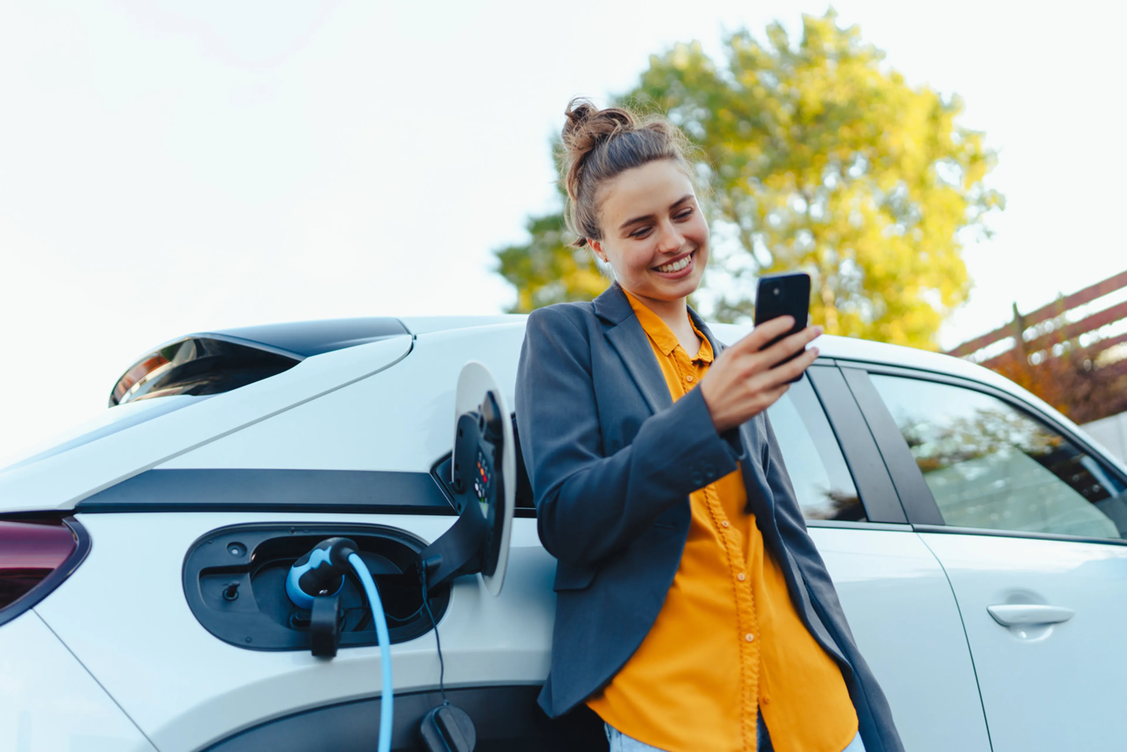 Frau lehnt an einem E-Auto mit einem Smartphone in der Hand