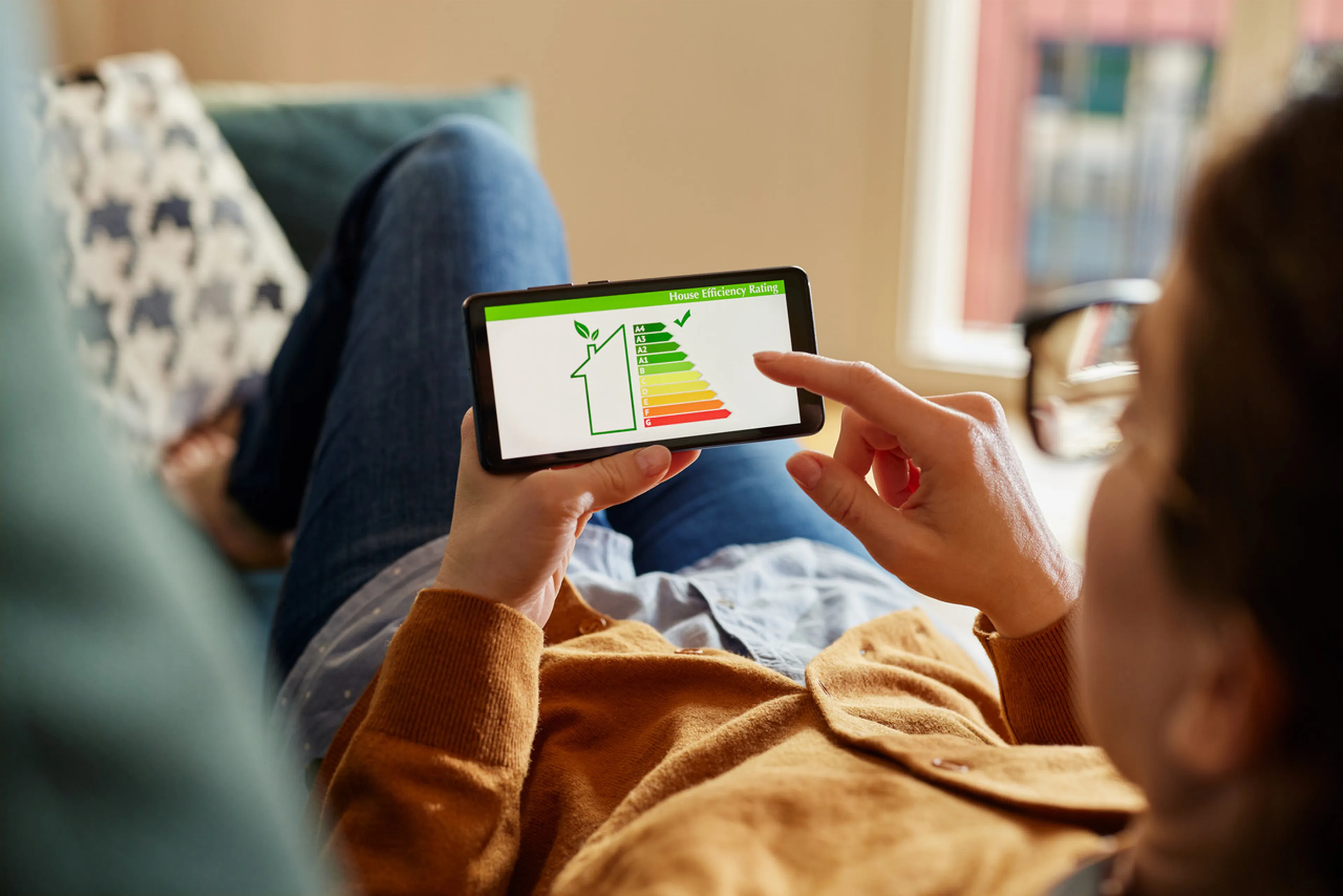 Person sitzt auf dem Sofa und sieht sich auf dem Smartphone eine Grafik zur Energieeffizienz an
