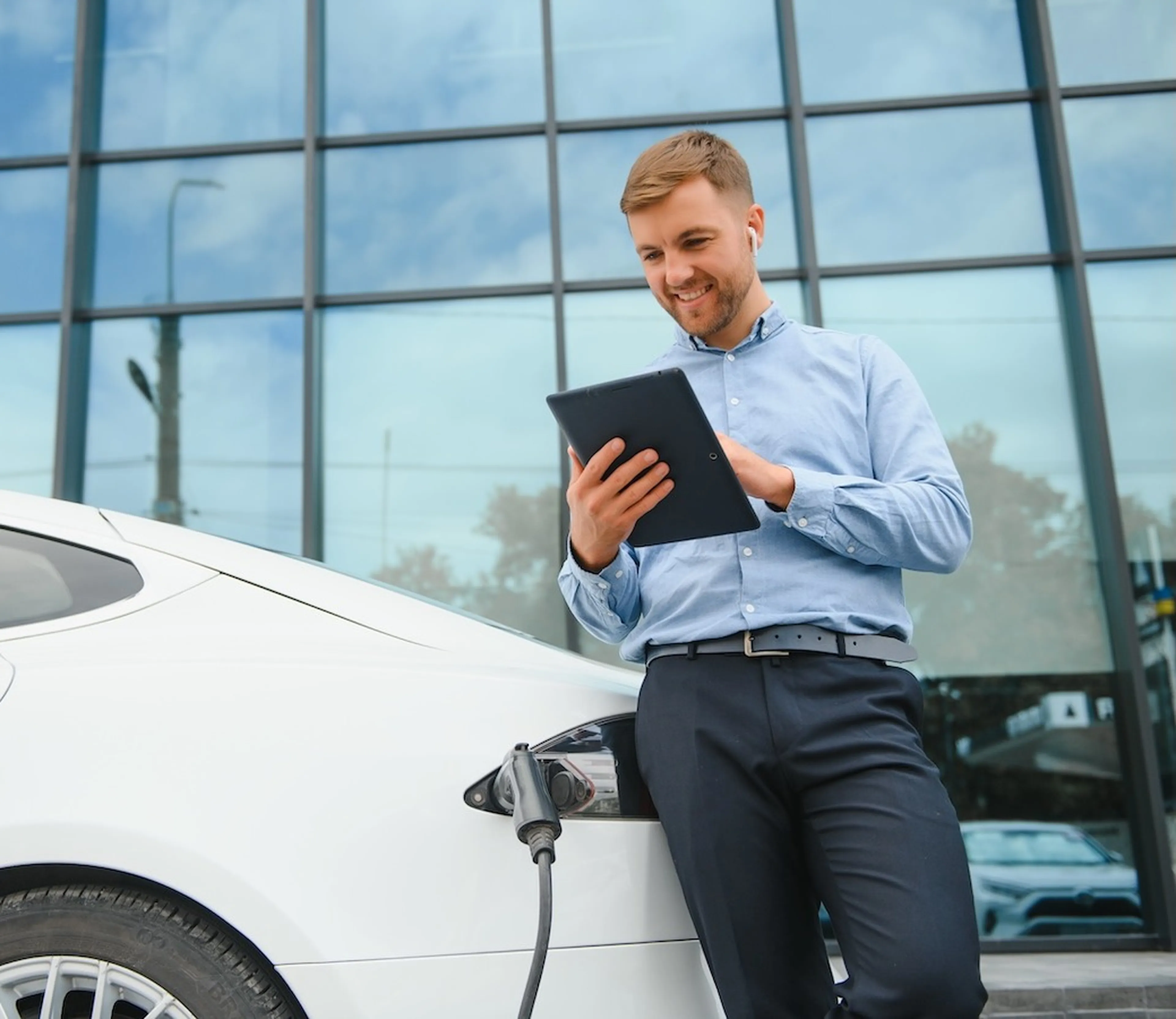 Mann steht vor einem ladenden E Auto, lächelt und schaut auf ein Tablet.