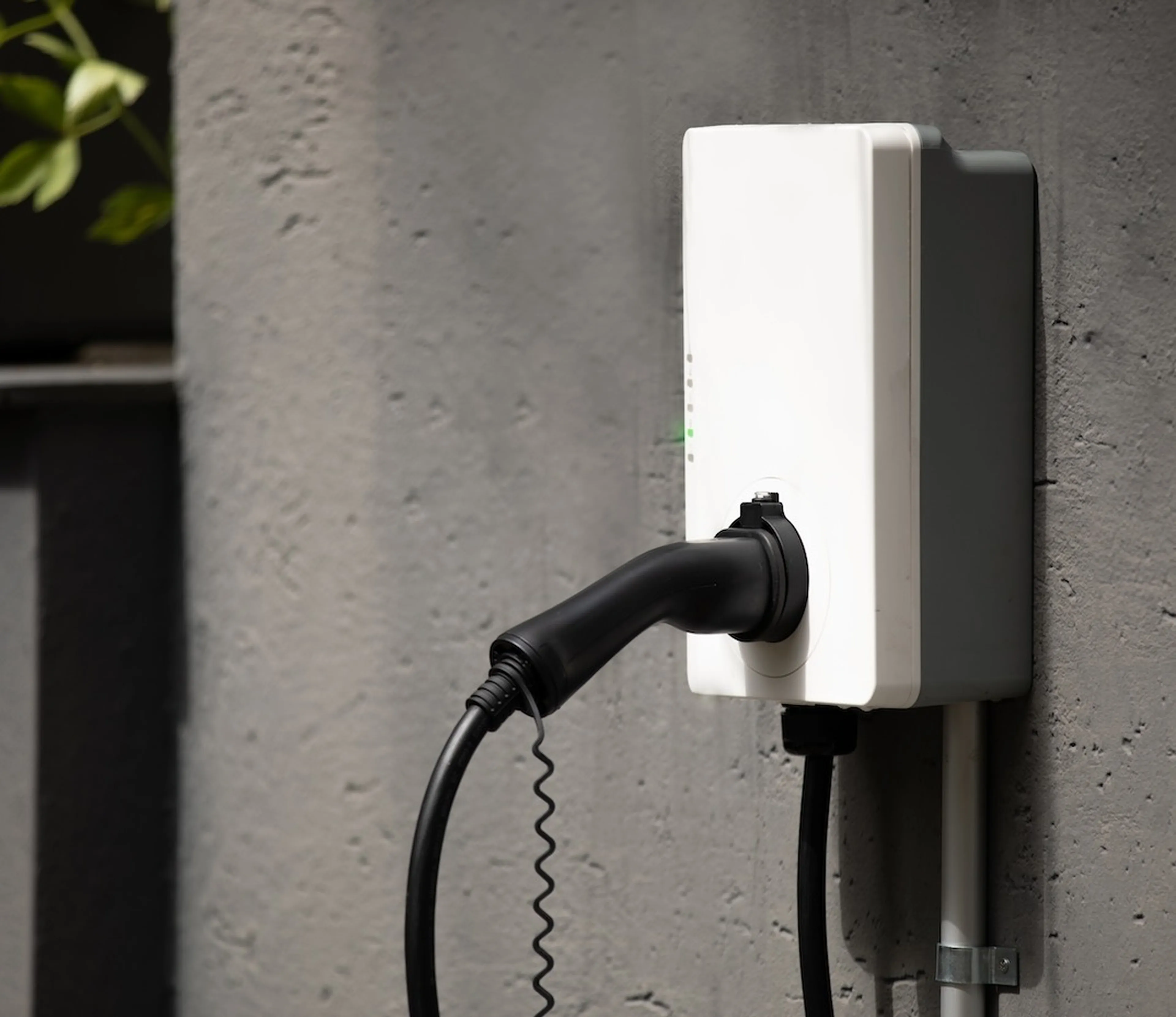 Weiße Wallbox mit Kabel an einer grauen Hauswand.