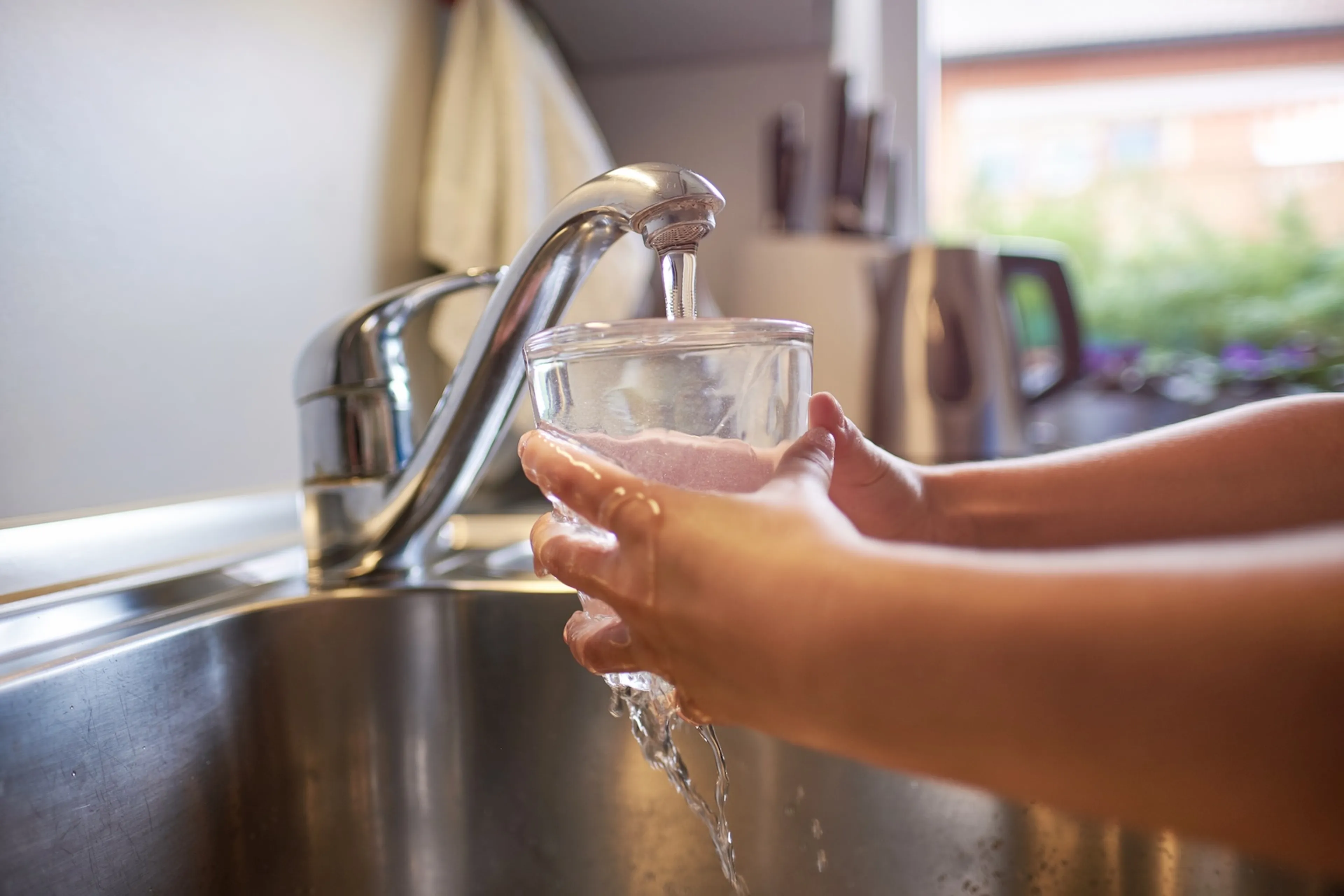 Person hält ein Glas unter den laufenden Wasserhahn.