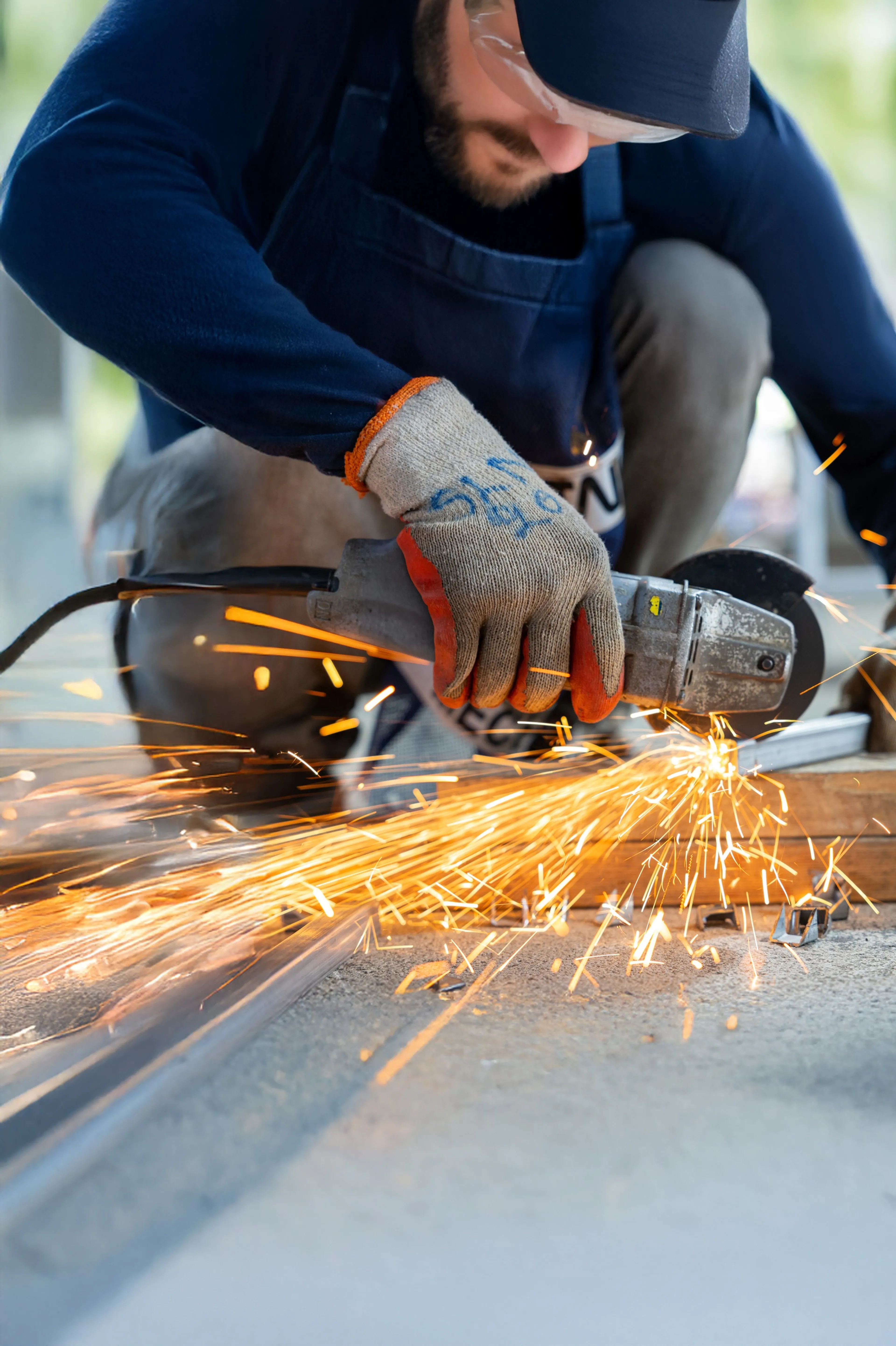 Handwerker mit Schutzkleidung arbeitet mit einem Trennschleifer und erzeugt Funken beim Schneiden eines Metallprofils.