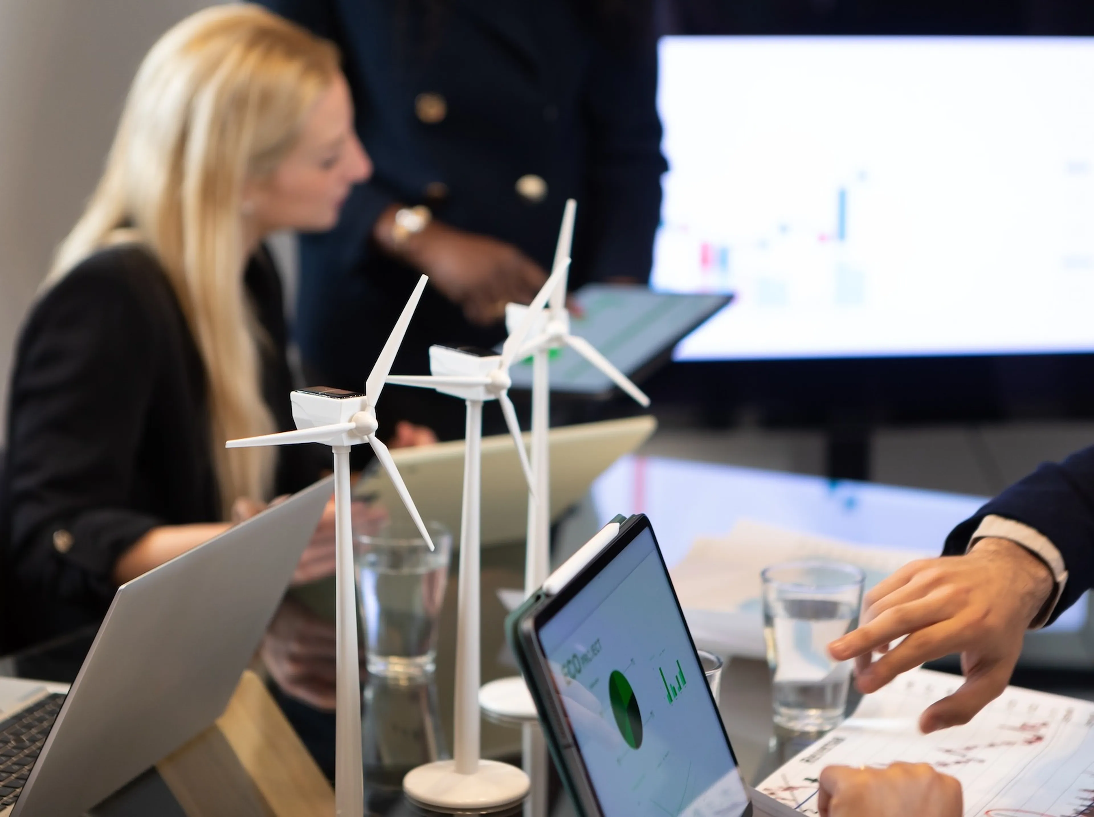 Menschen in einem Meeting mit Fokus auf Windkraft-Modelle und Nachhaltigkeitsdiagrammen auf Laptops.