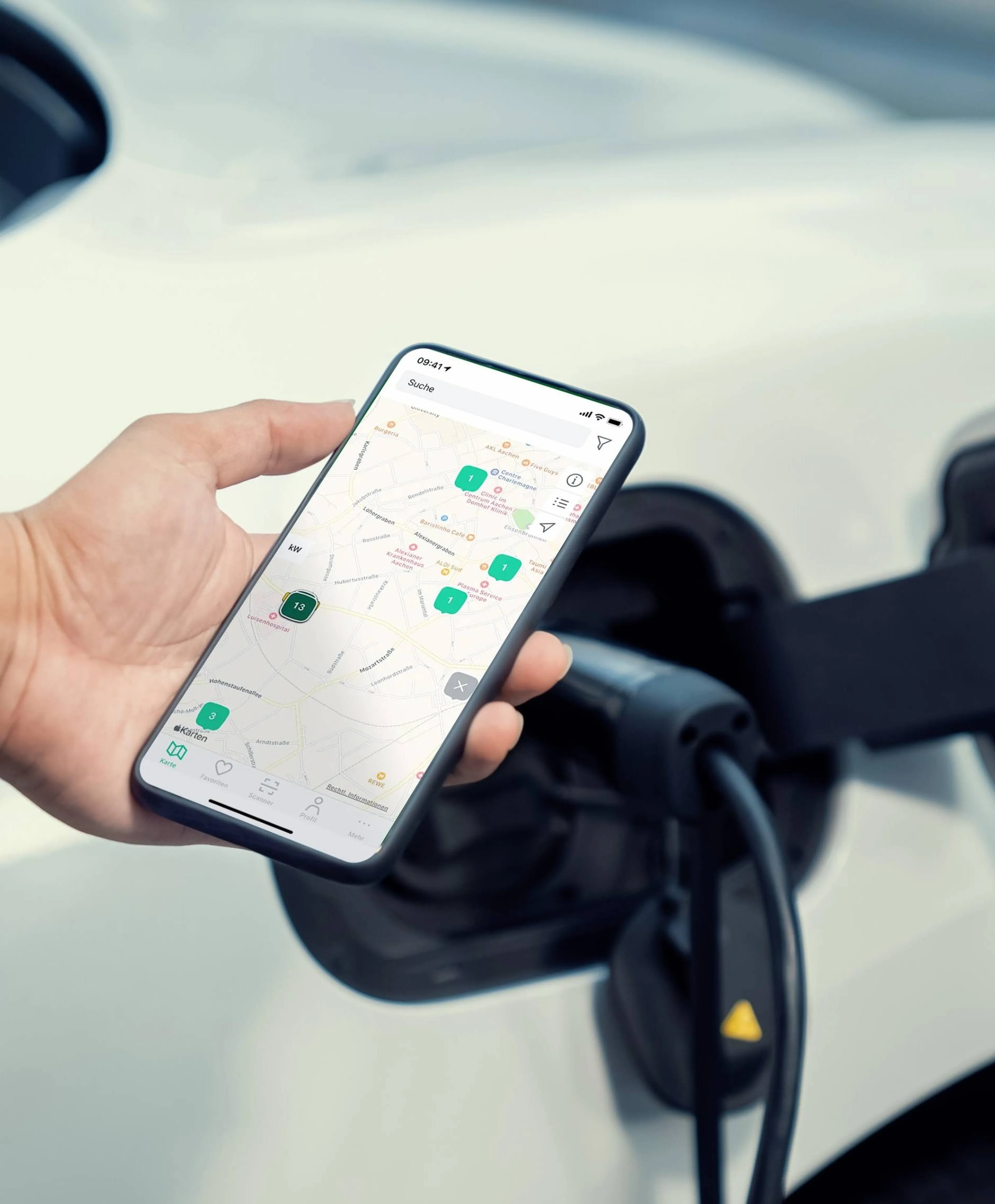 Eine Hand hält ein Smartphone, auf dem LAdestationen auf einer Karte zu sehen sind. Im Hintergrund läd ein E Auto.