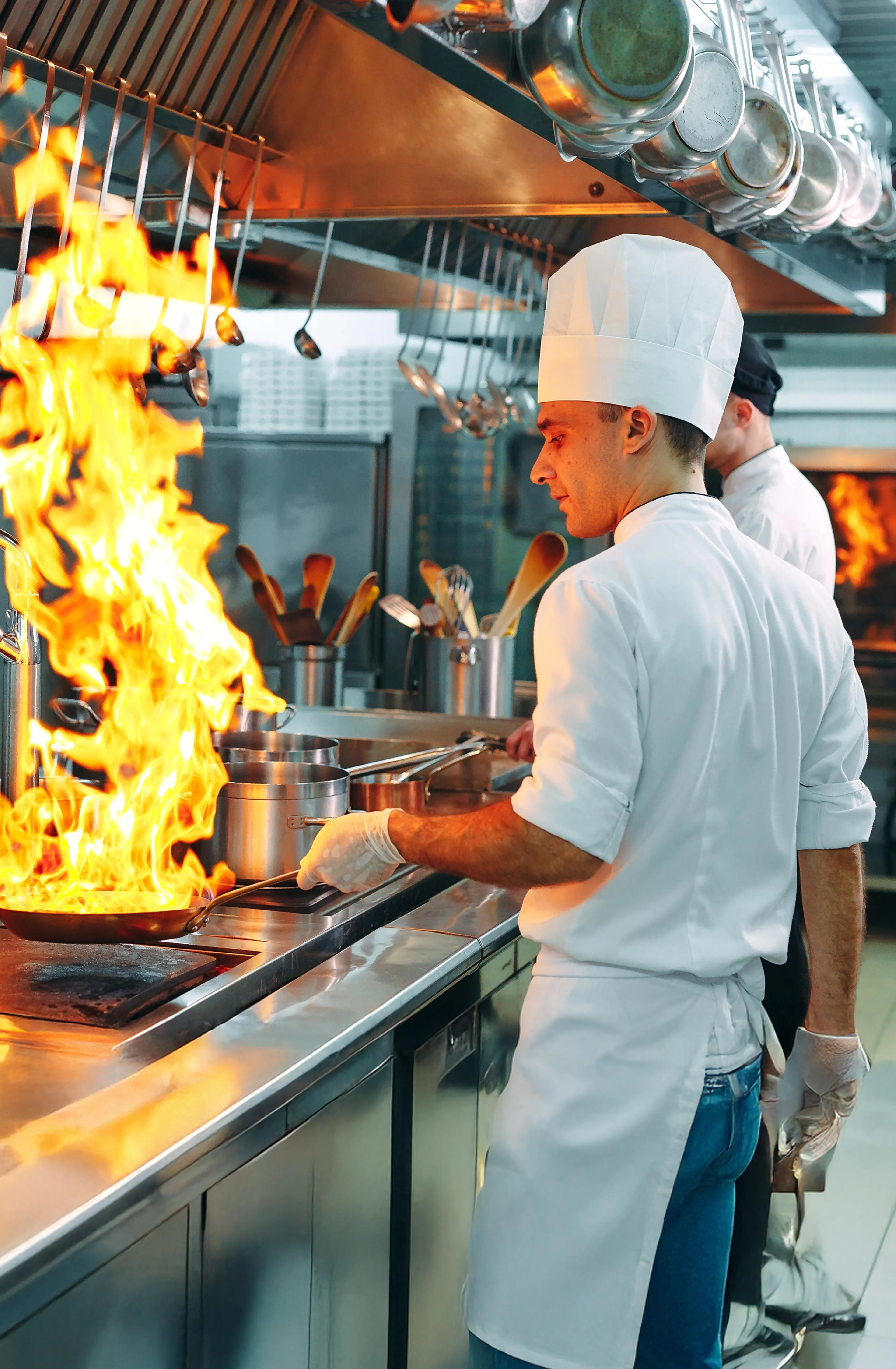 Koch in professioneller Großküche mit großer Gasflamme beim Braten am Herd