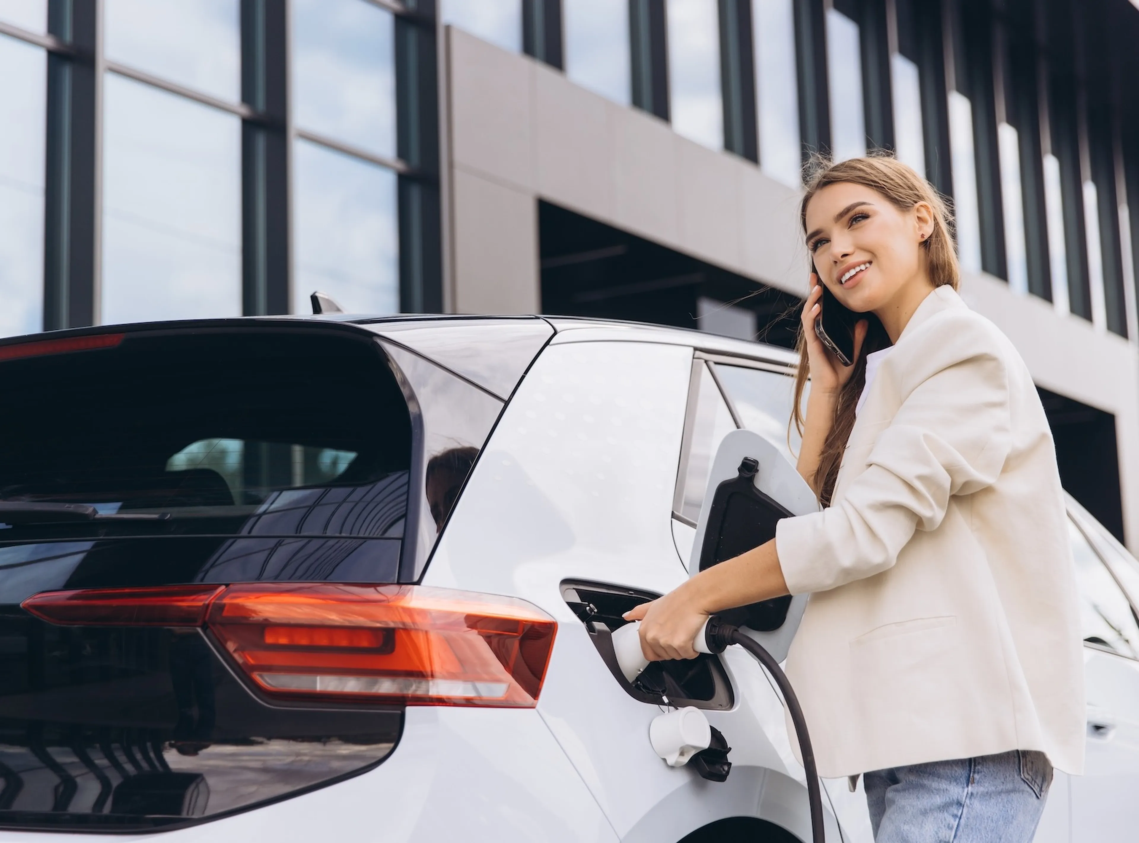 Frau läd ihr E Auto vor einem Gebäude und telefoniert dabei.