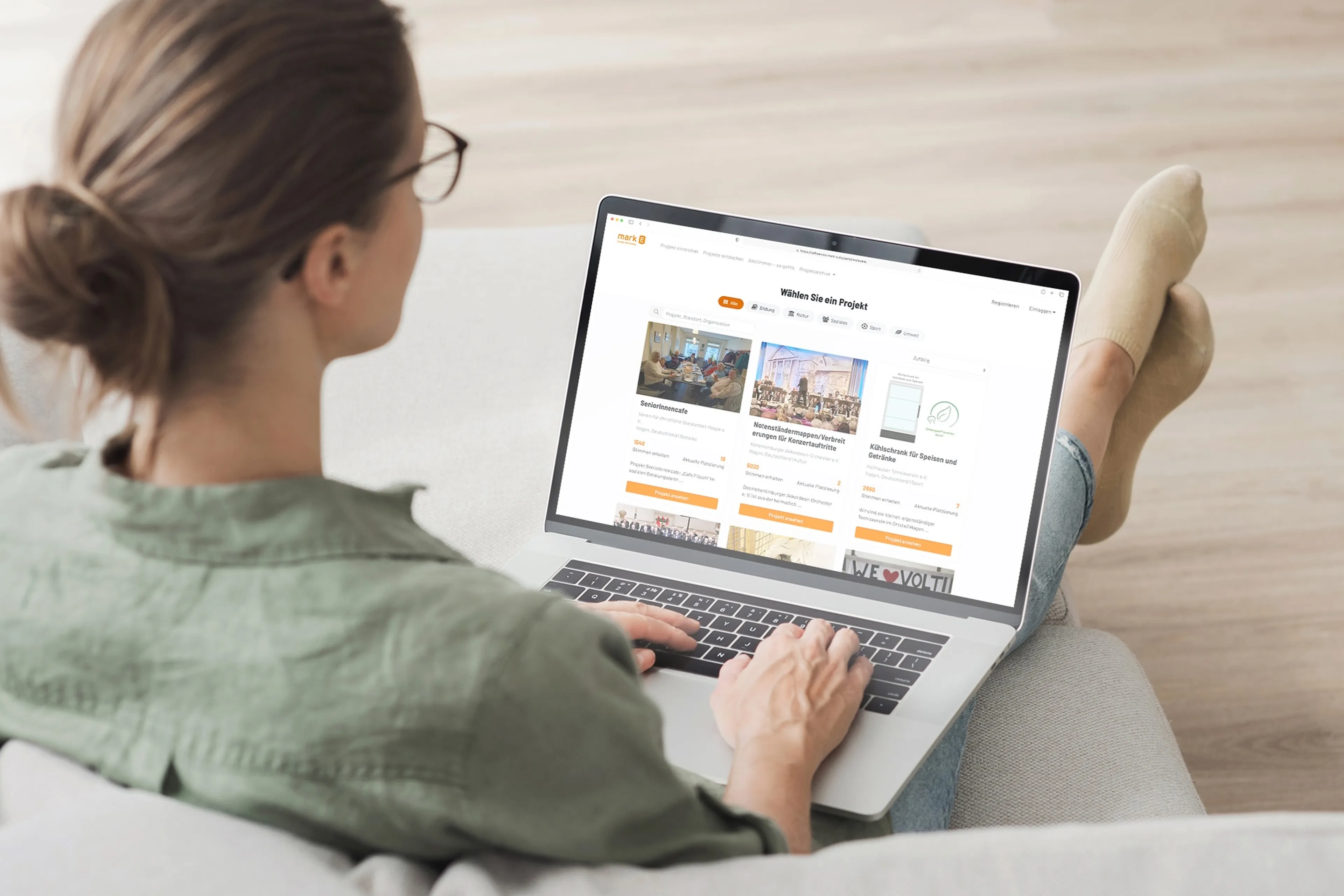 Eine Frau sitz auf dem Sofa und hat auf ihrem Schoß einen Laptop. Auf dem Laptop sind die Projekte sichtbar.