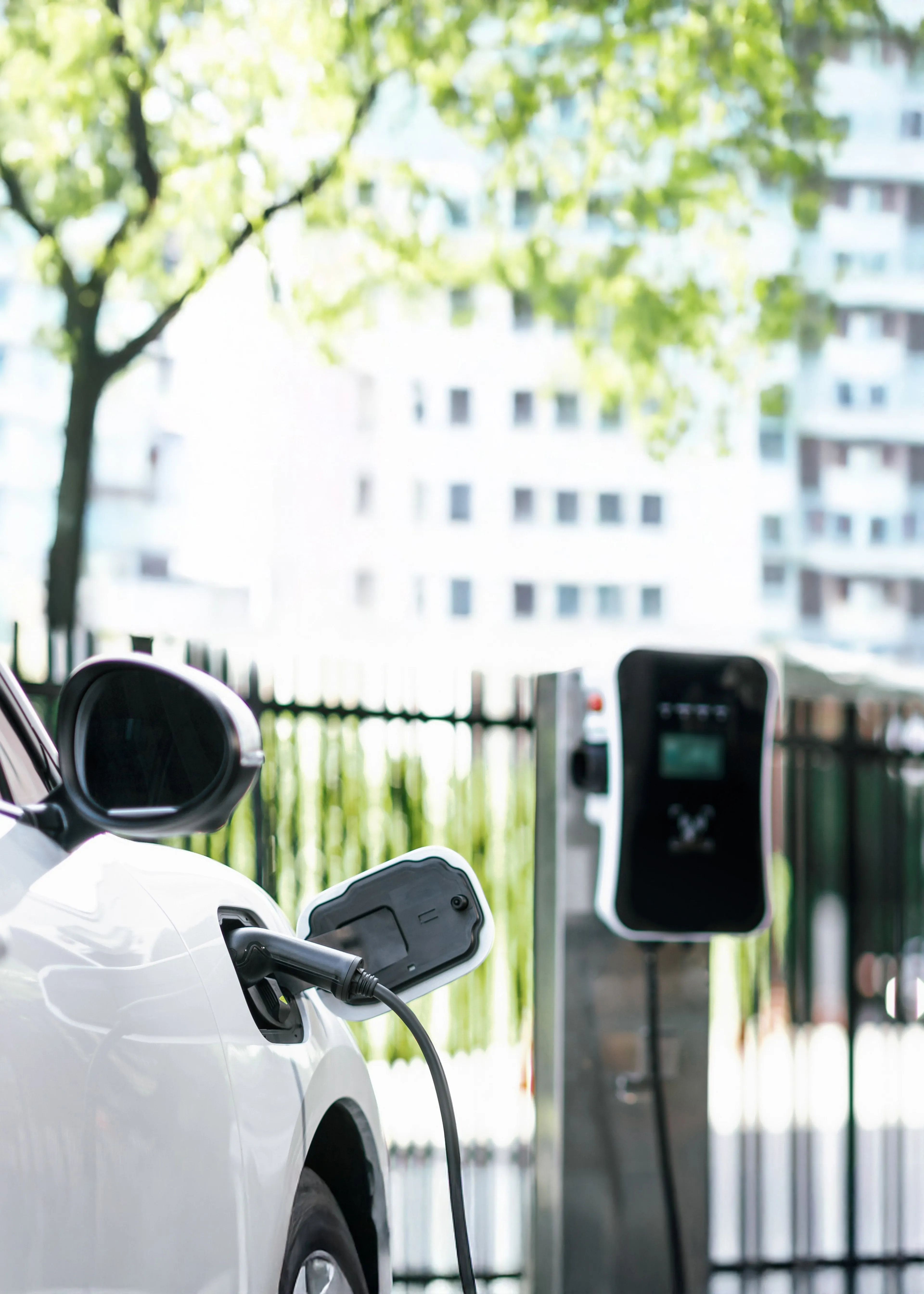 E auto lädt an einer nicht-öffentlichen Ladesäule im Freien. Im Hintergrund sind Wohnhäuser und grüne Bäume zu sehen.