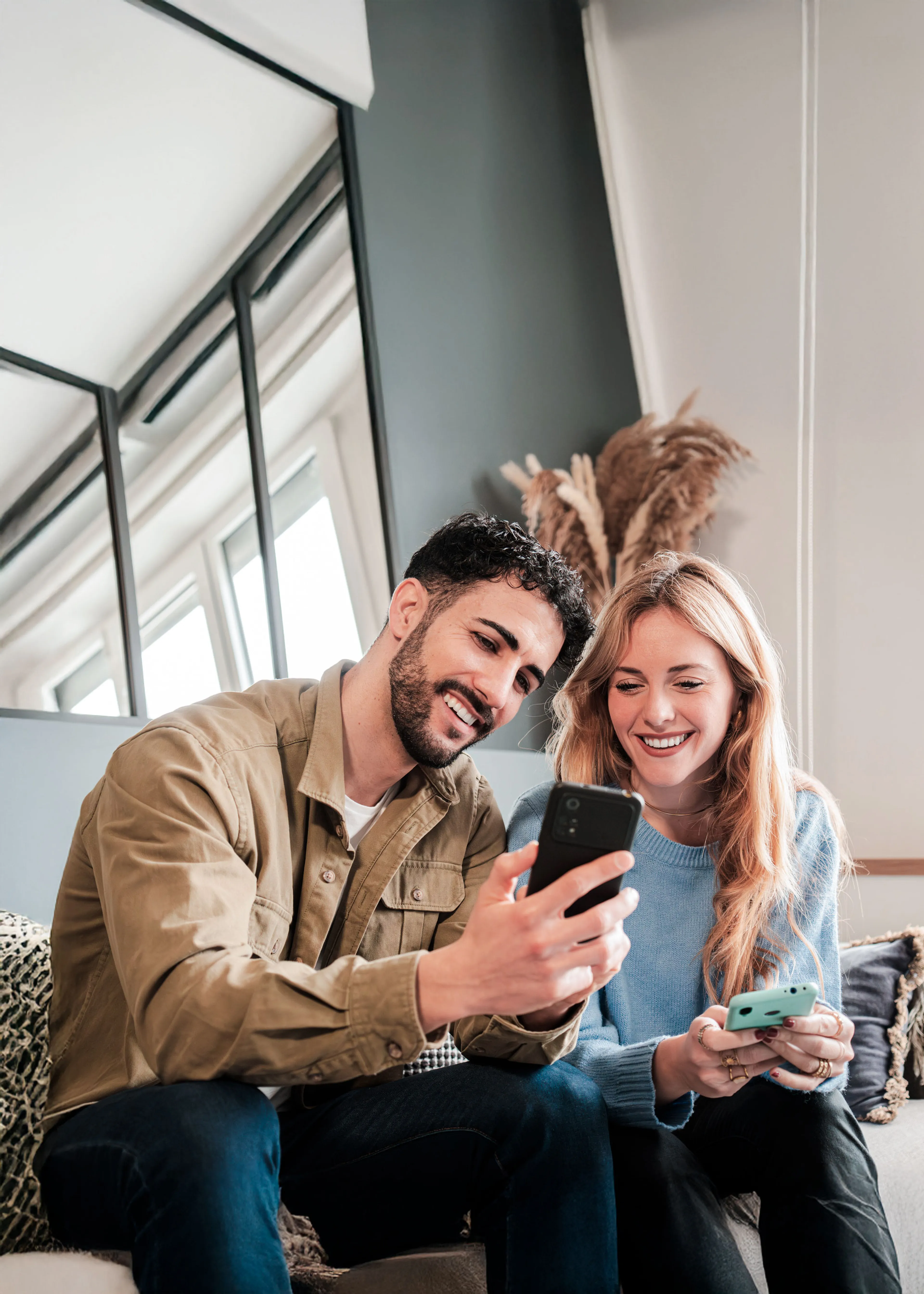 So einfach geht Kunden werben: Ein junger Mann auf der Couch sitzend zeigt einer Freundin daneben auf dem Smartphone wie er sie als Kundin werben kann.