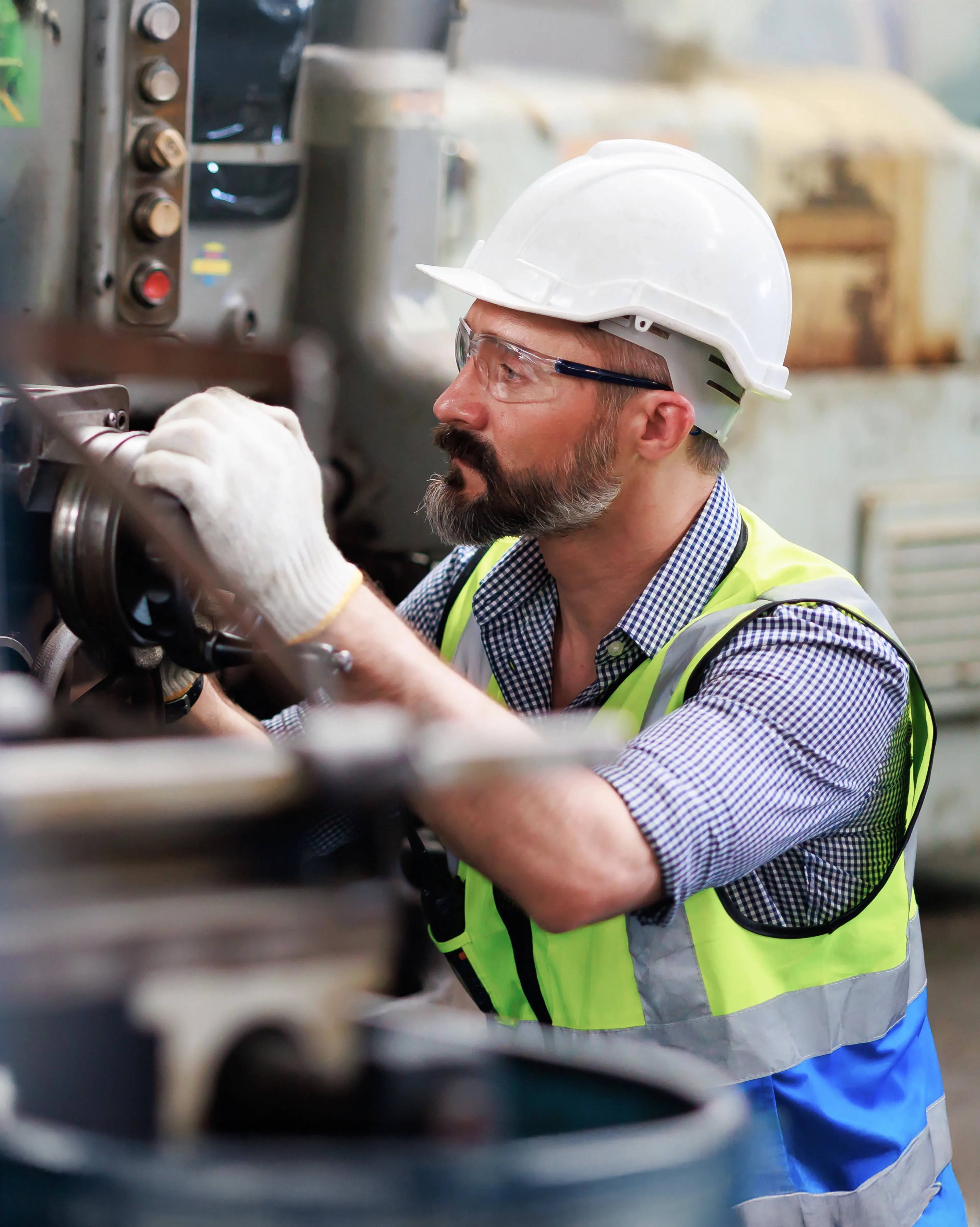 Industriemitarbeiter mit Schutzhelm und Warnweste wartet eine große Maschine in einer Produktionshalle.