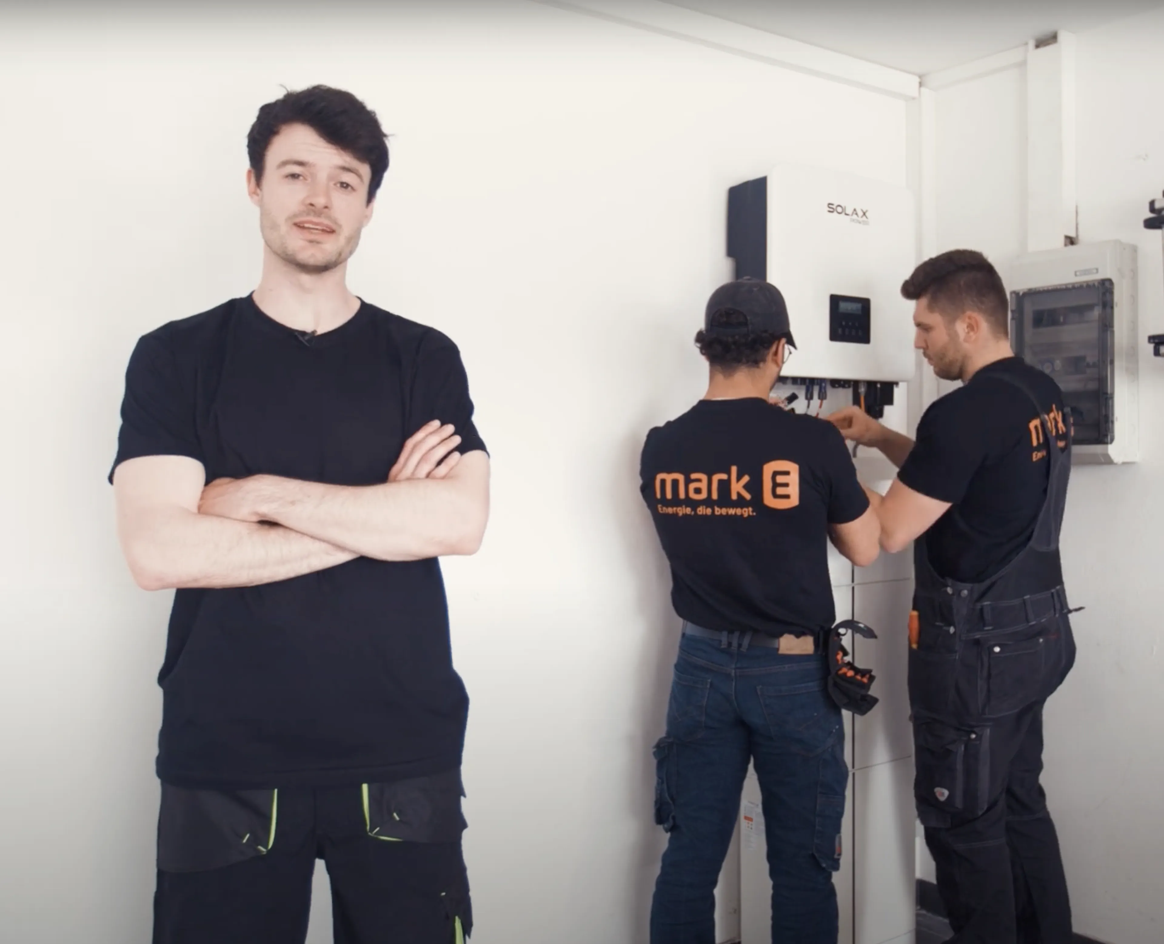 Zwei Monteure von Mark-E installieren einen Wechselrichter für eine Solaranlage, ein Kollege steht im Vordergrund