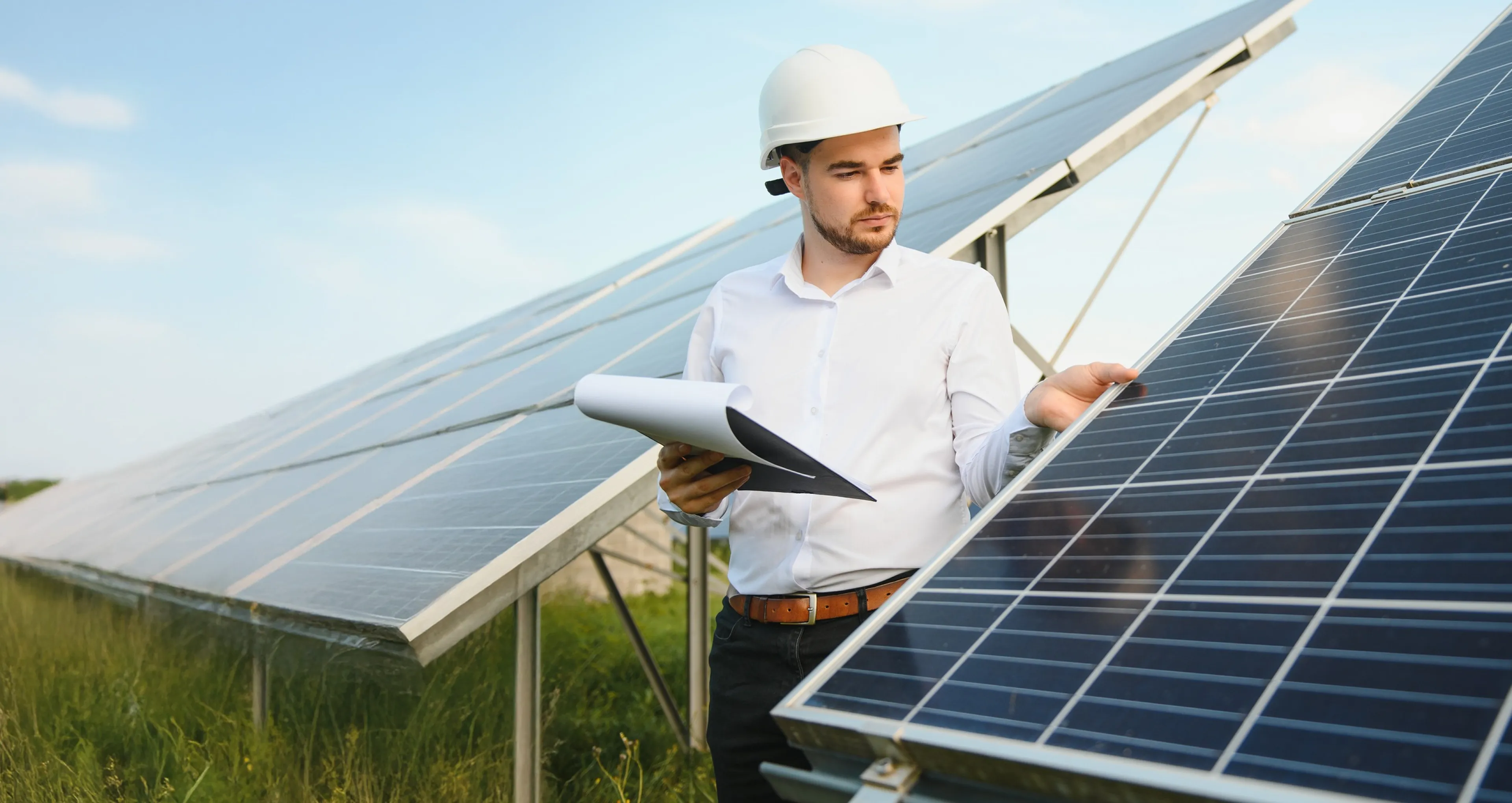 Techniker mit Helm und Dokumentenmappe inspiziert Solarpanels im Freien bei klarem Himmel