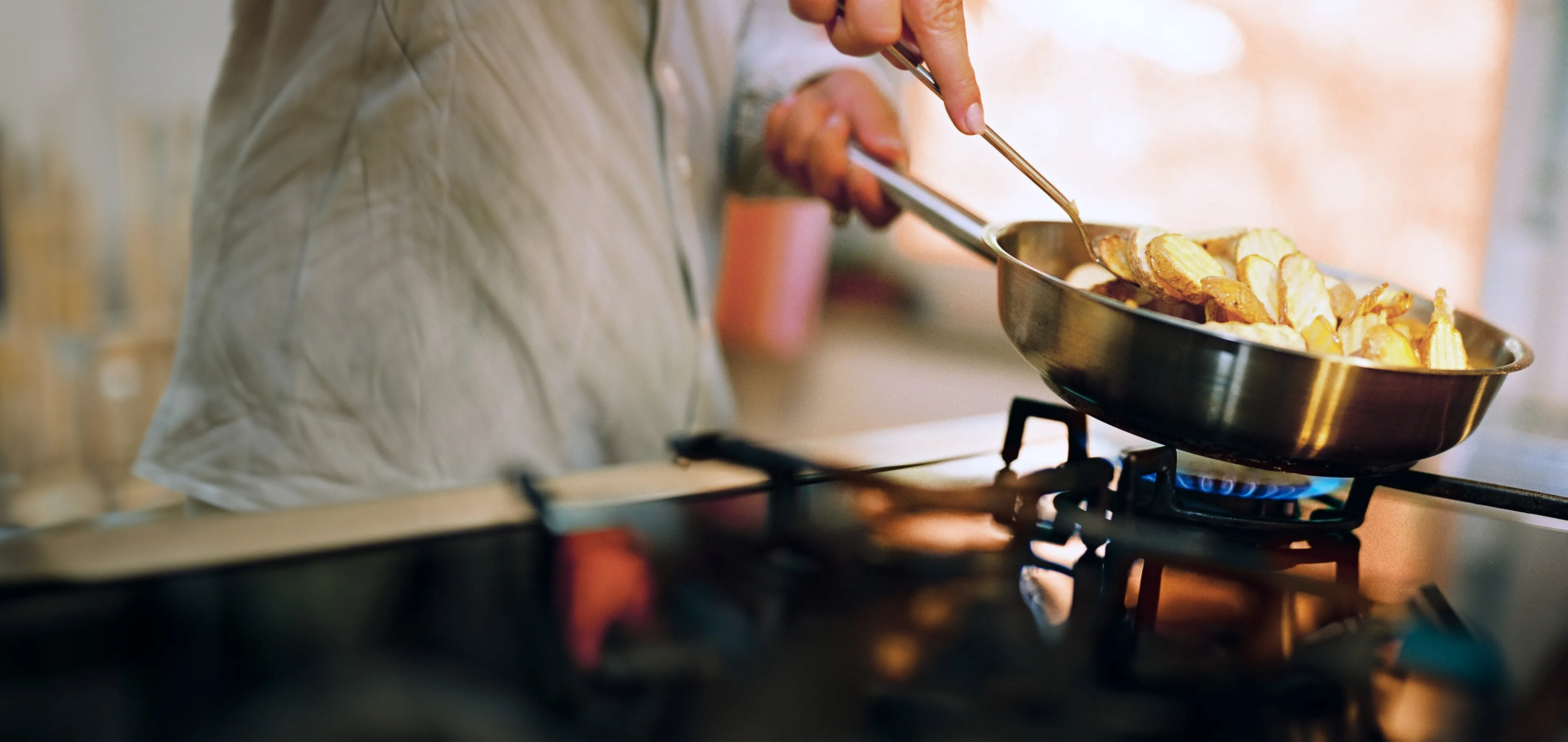 Person brät Kartoffeln in einer Pfanne über einem Gasherd an.