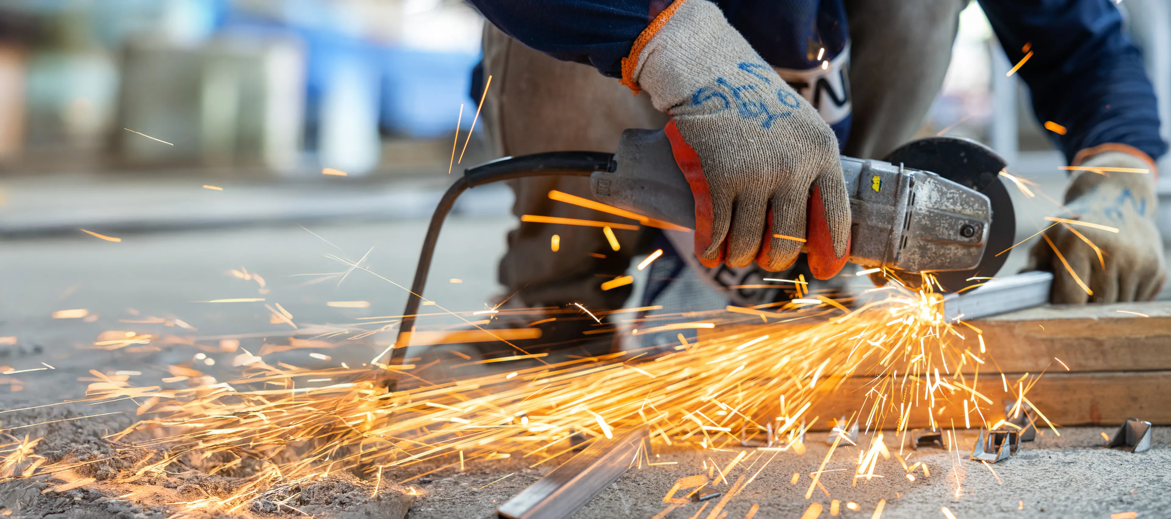 Nahaufnahme eines Arbeiters mit Schutzhandschuhen beim Schneiden von Metall mit einer Trennschleifmaschine. Funken fliegen durch die Luft.