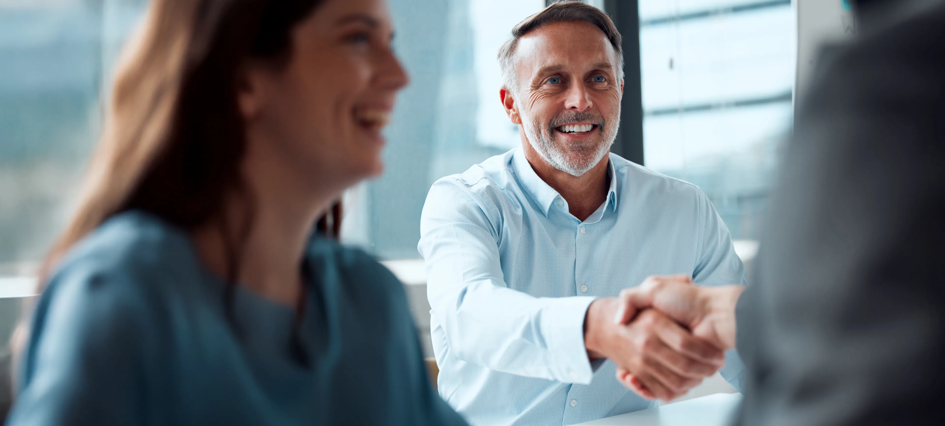 Ein Mann in einem hellblauen Hemd lächelt und reicht einer anderen Person die Hand zum Vertragsabschluss beim Energiehandel.