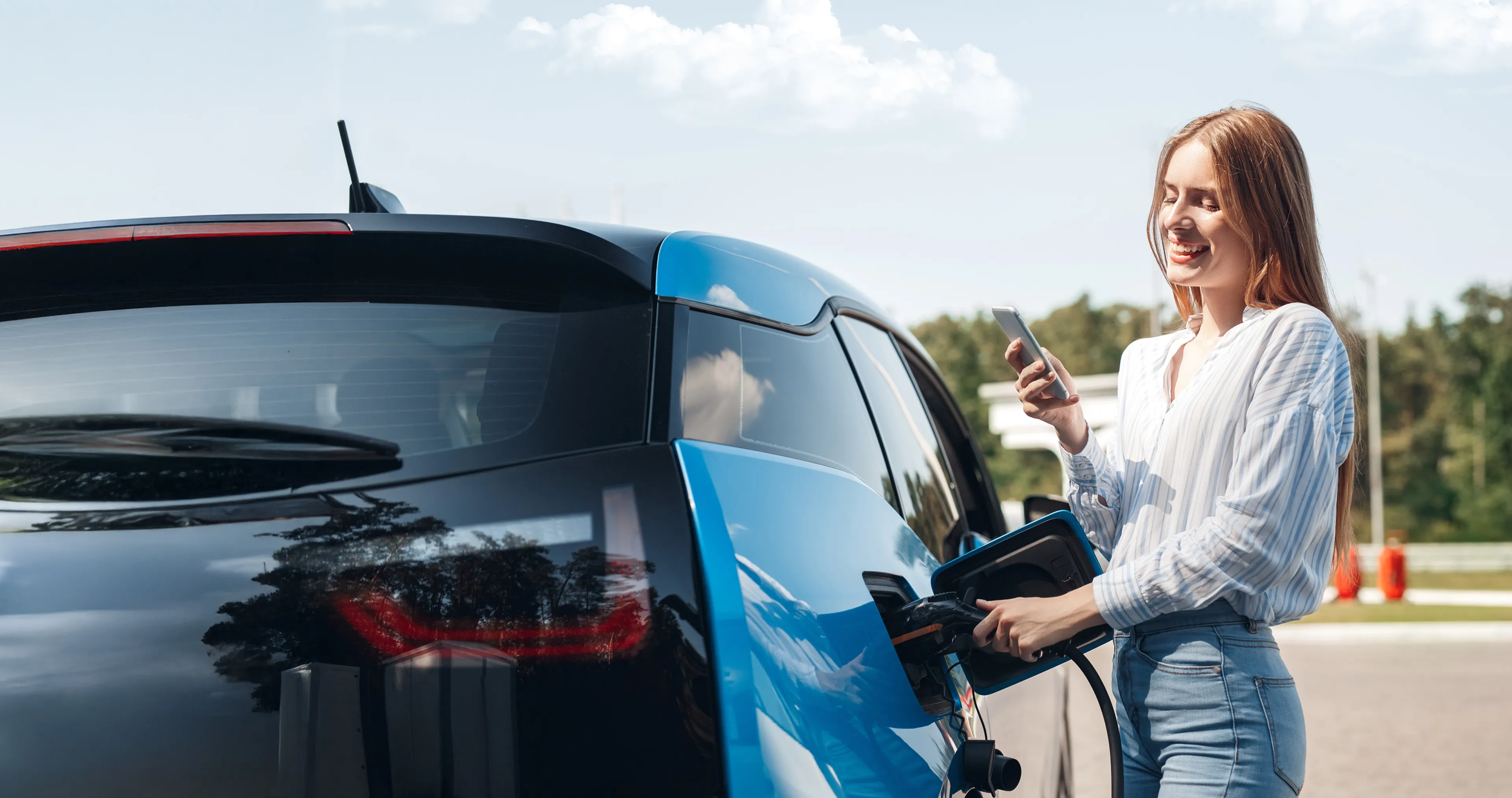 Frau lädt lächelnd ihr E-Auto mit Smartphone in der Hand