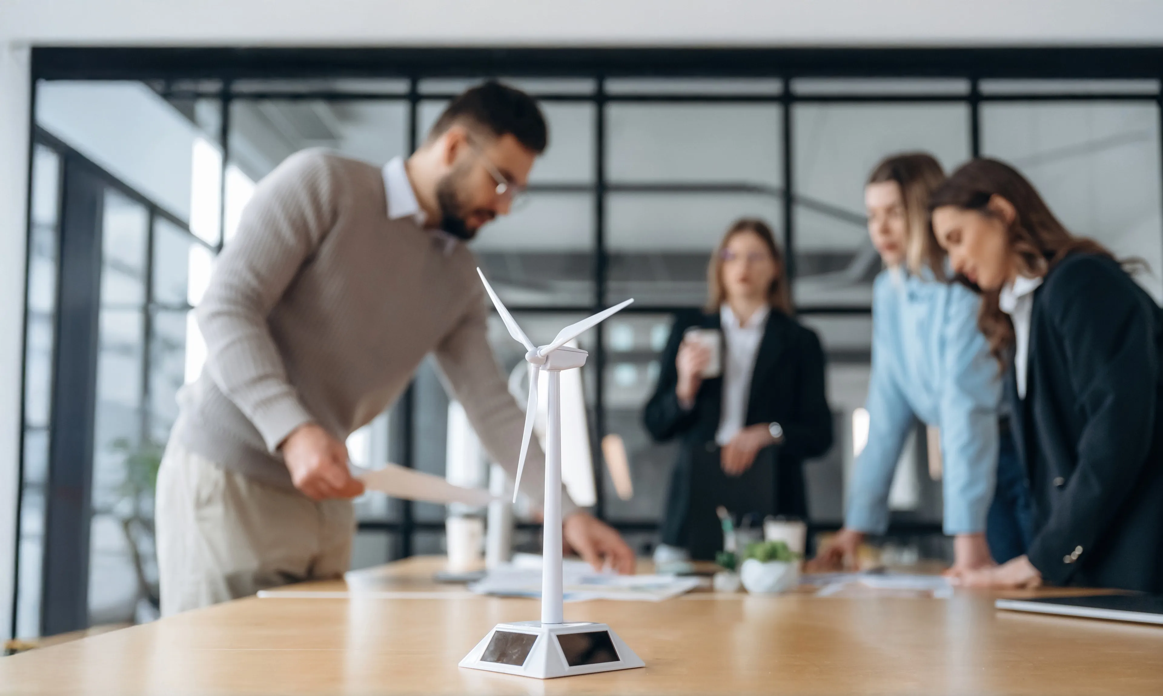 Gruppe von vier Personen in einem modernen Büro bei einer Besprechung mit einem Windradmodell auf dem Tisch im Vordergrund.