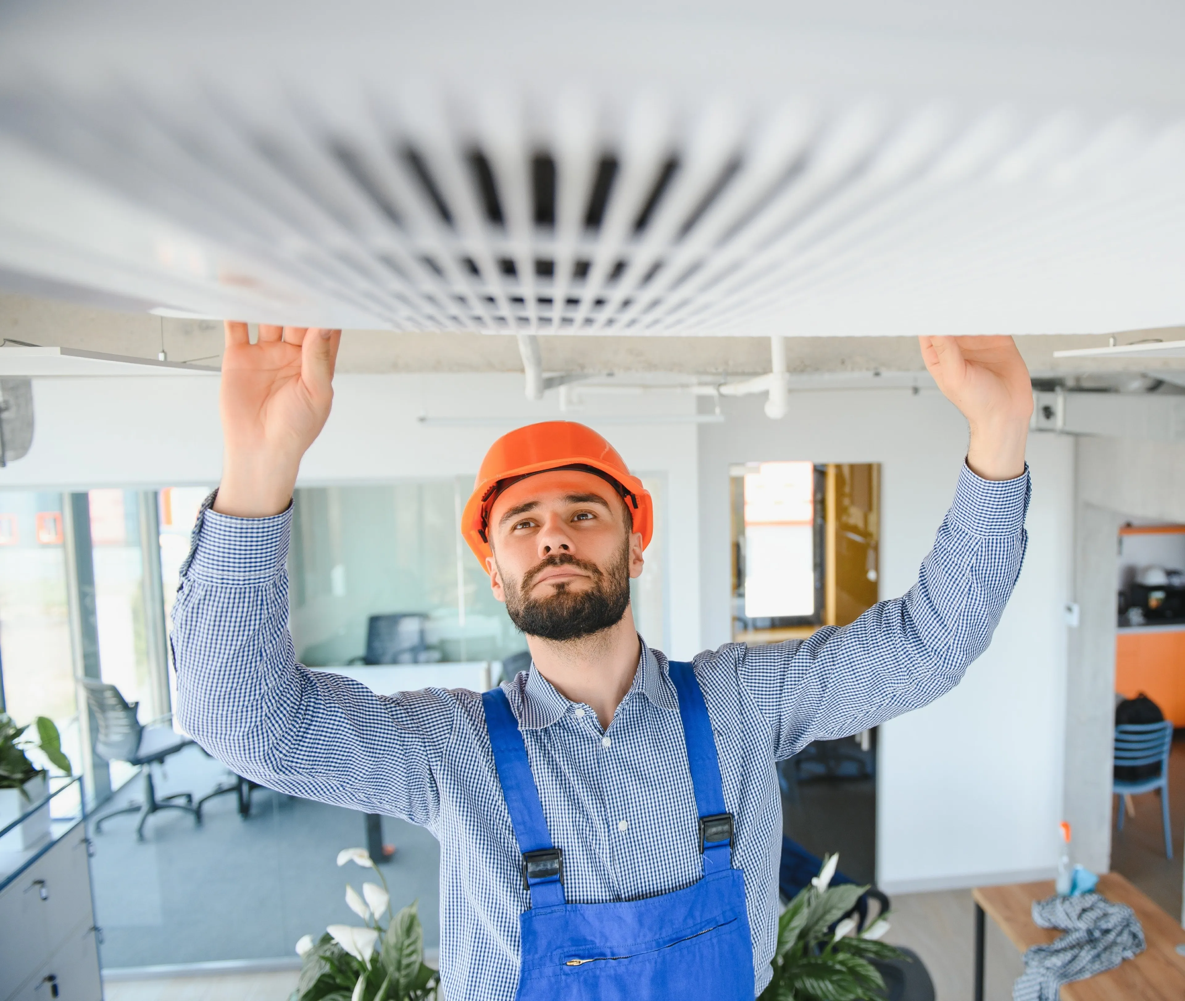 Techniker mit Helm überprüft eine Klimaanlage an der Decke in einem modernen Büro