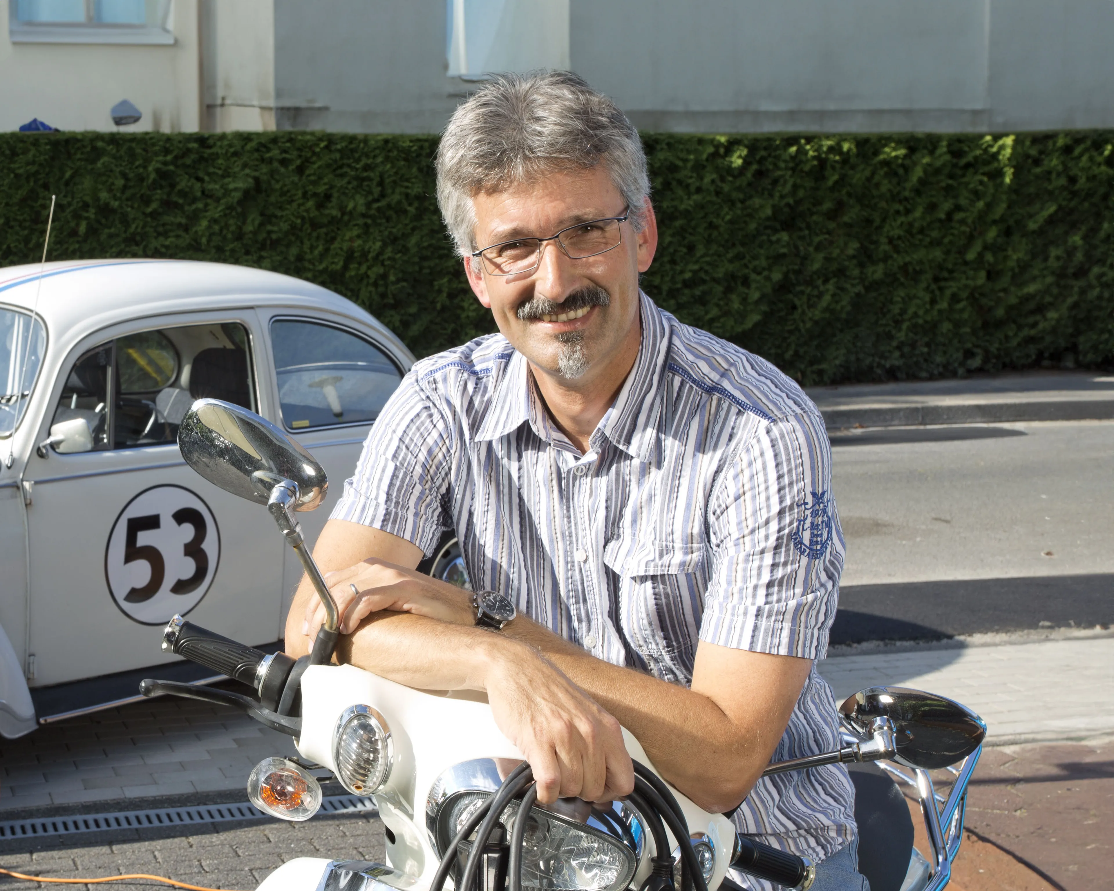Volker Haá mit Elektroroller vor umgerüstetem VW Käfer mit Ladekabel