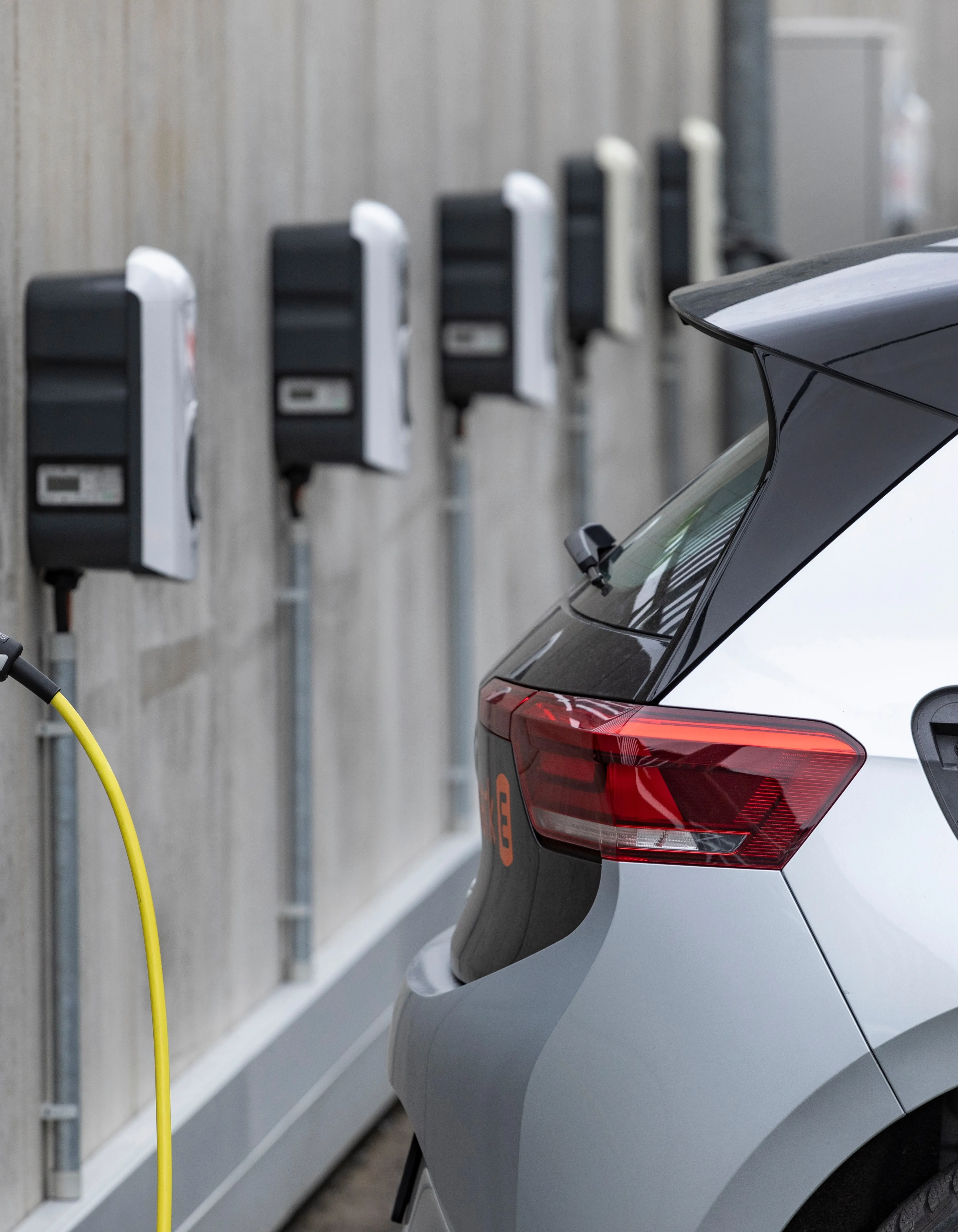 Aufladen eines Elektroautos an einer Station mit mehreren Ladegeräten an einer Betonwand, mit einem gelben Ladekabel.