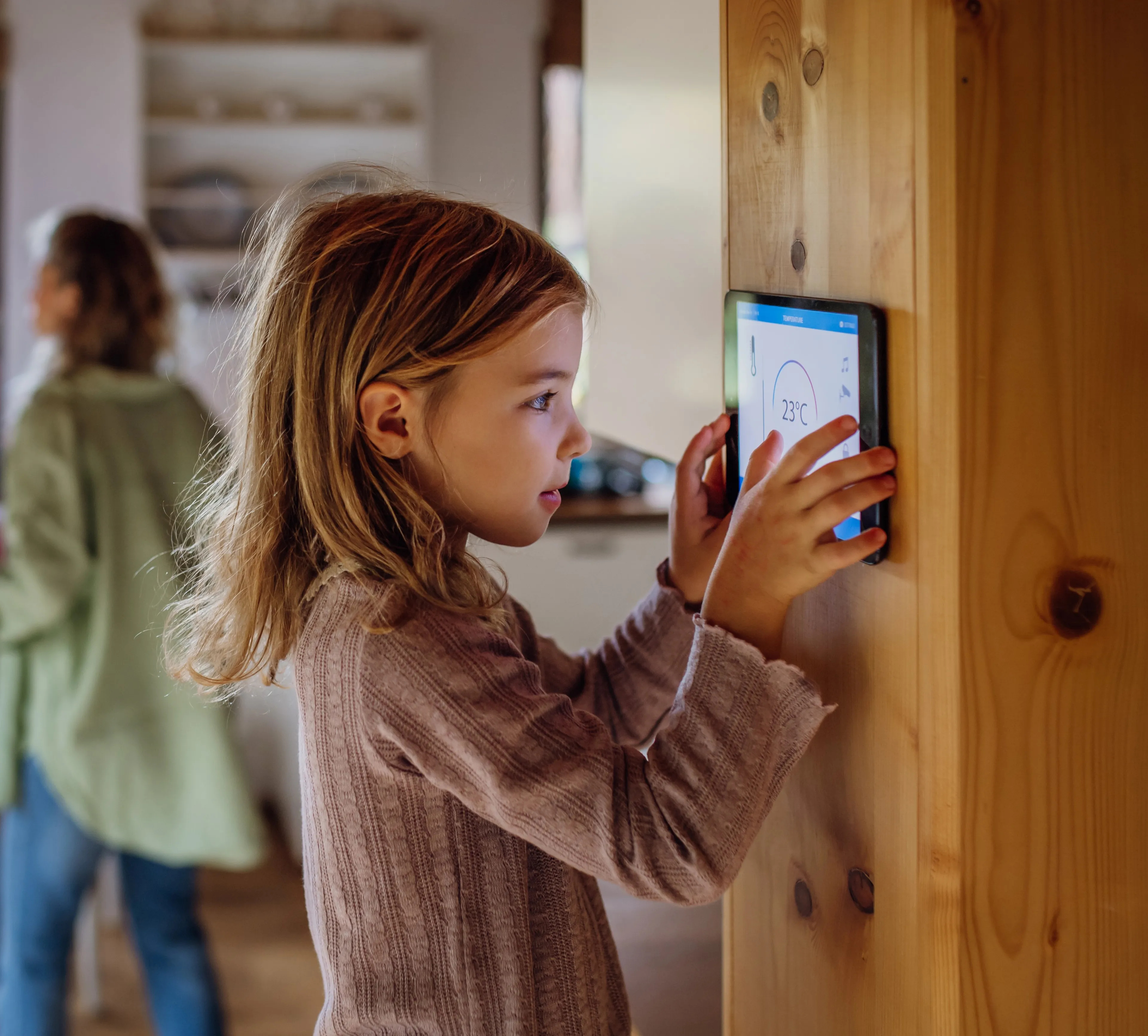 Mädchen reguliert die Raumtemperatur über ein Smart-Home-Display – effizient heizen mit Wärmepumpen Strom von Mark-E.