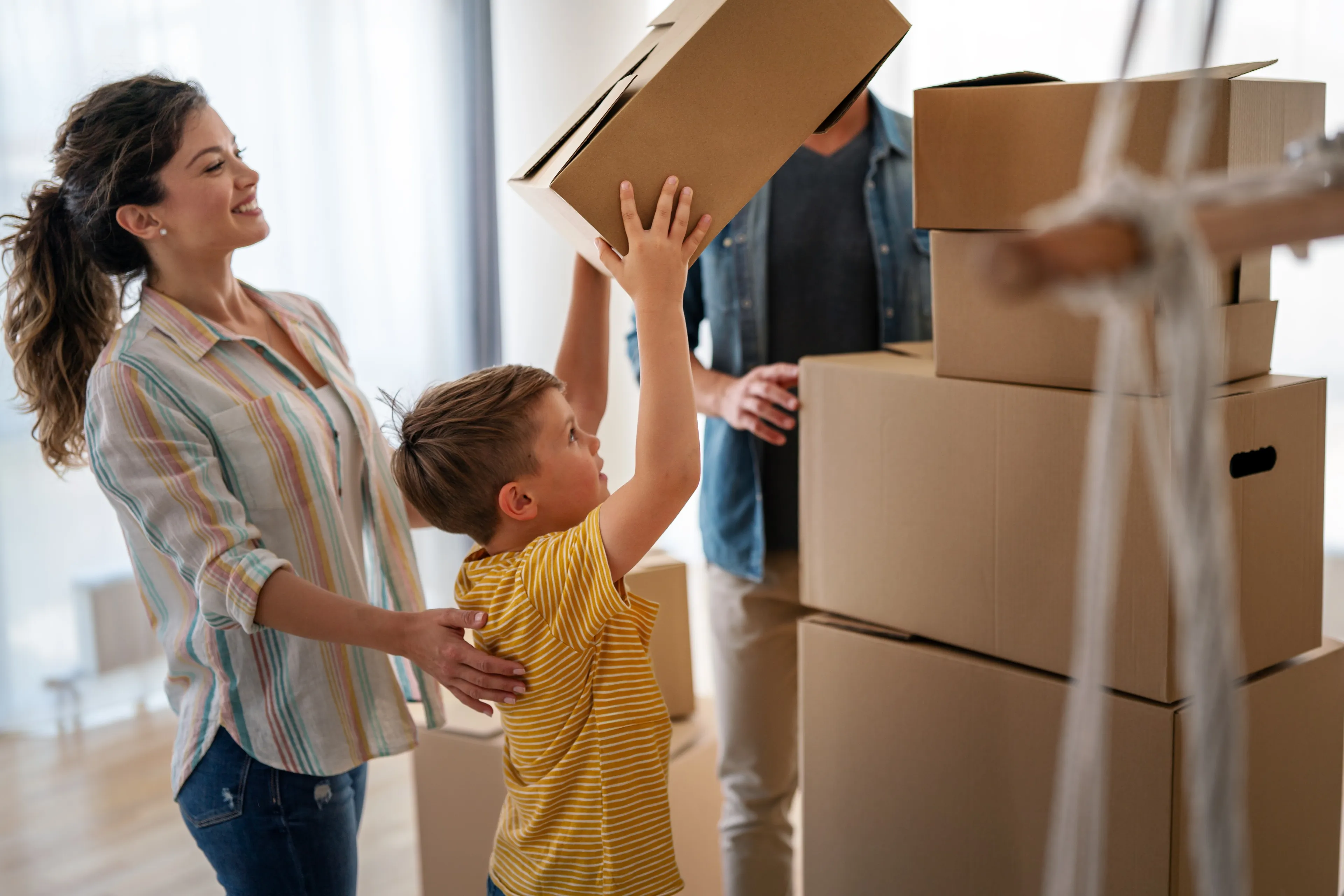 Familie mit Kind hebt Umzugskarton im neuen Zuhause
