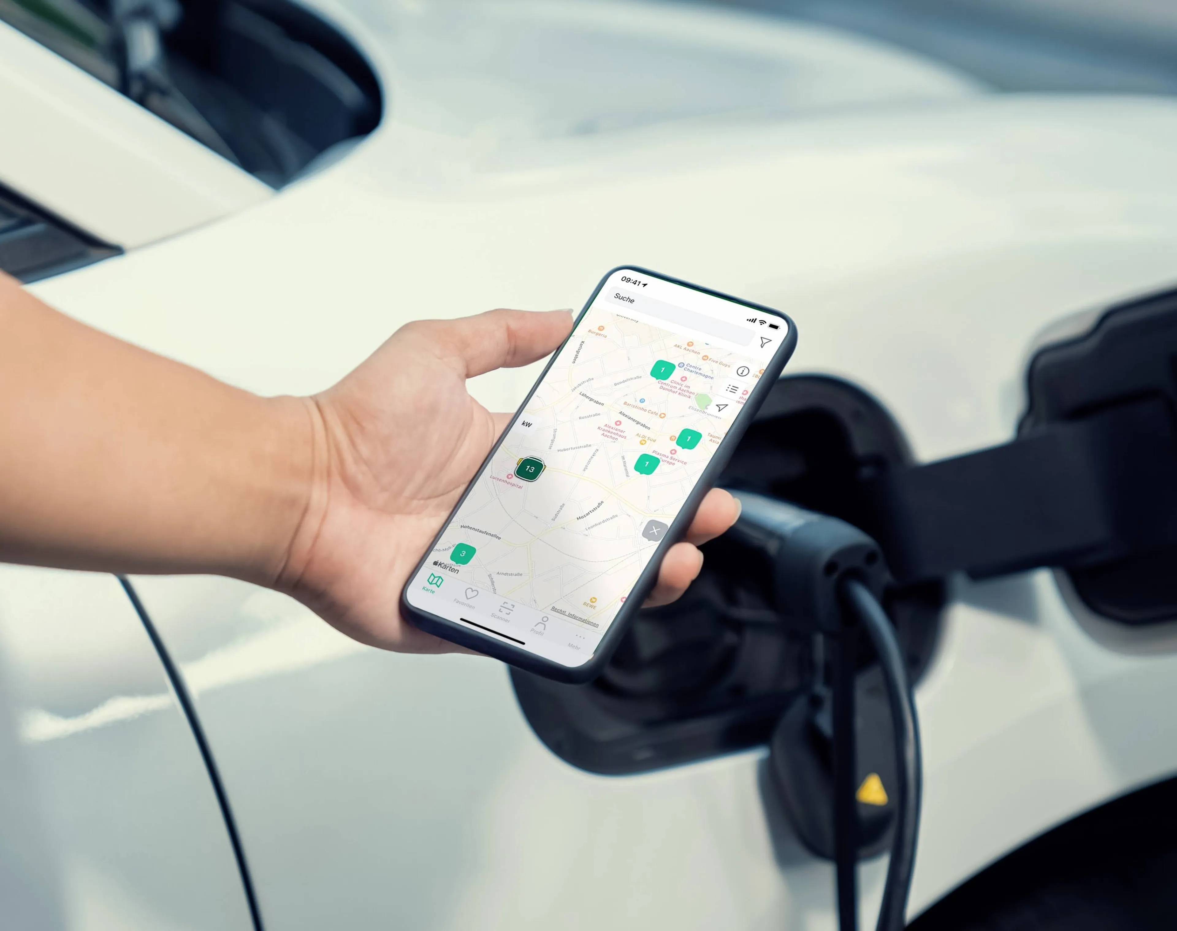 Eine Hand hält ein Smartphone neben einem Elektroauto, welches gerade lädt. Es sind verschiedene Ladestationen zu sehen.