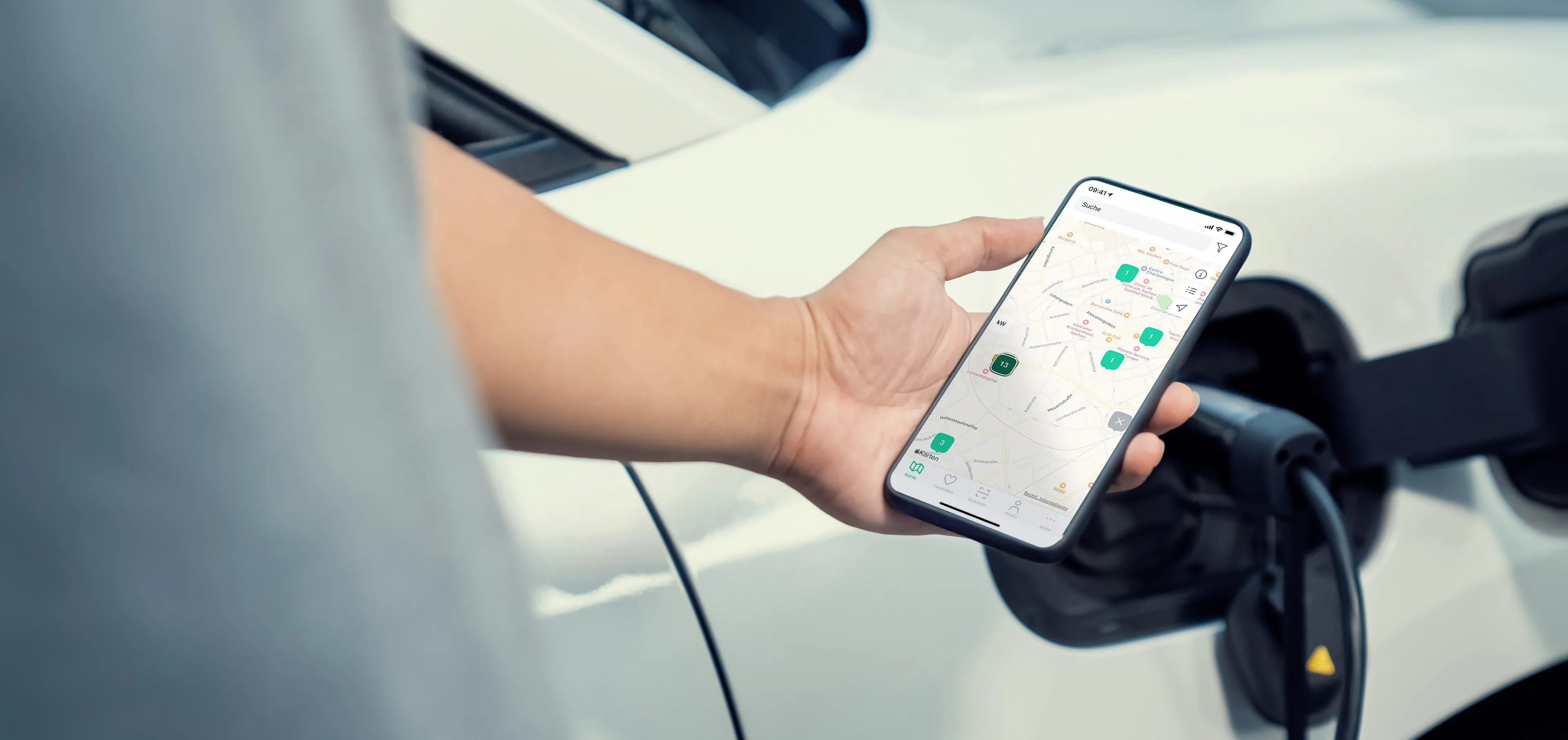 Eine Person hält ein Smartphone mit einer Karten-App in der Nähe eines Elektroautos, das aufgeladen wird.