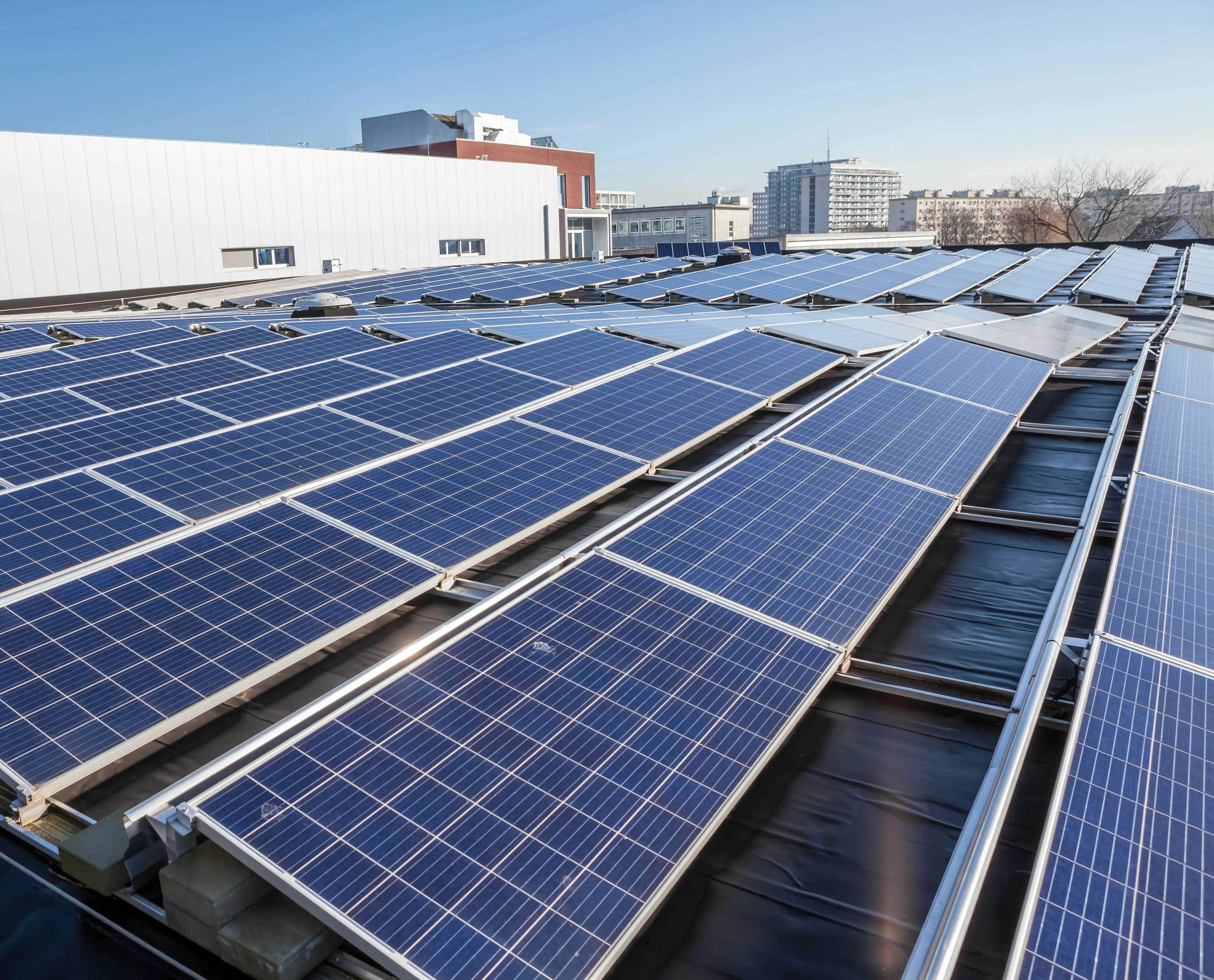 Solarmodule auf dem Dach unter blauem Himmel, mit städtischen Gebäuden im Hintergrund.
