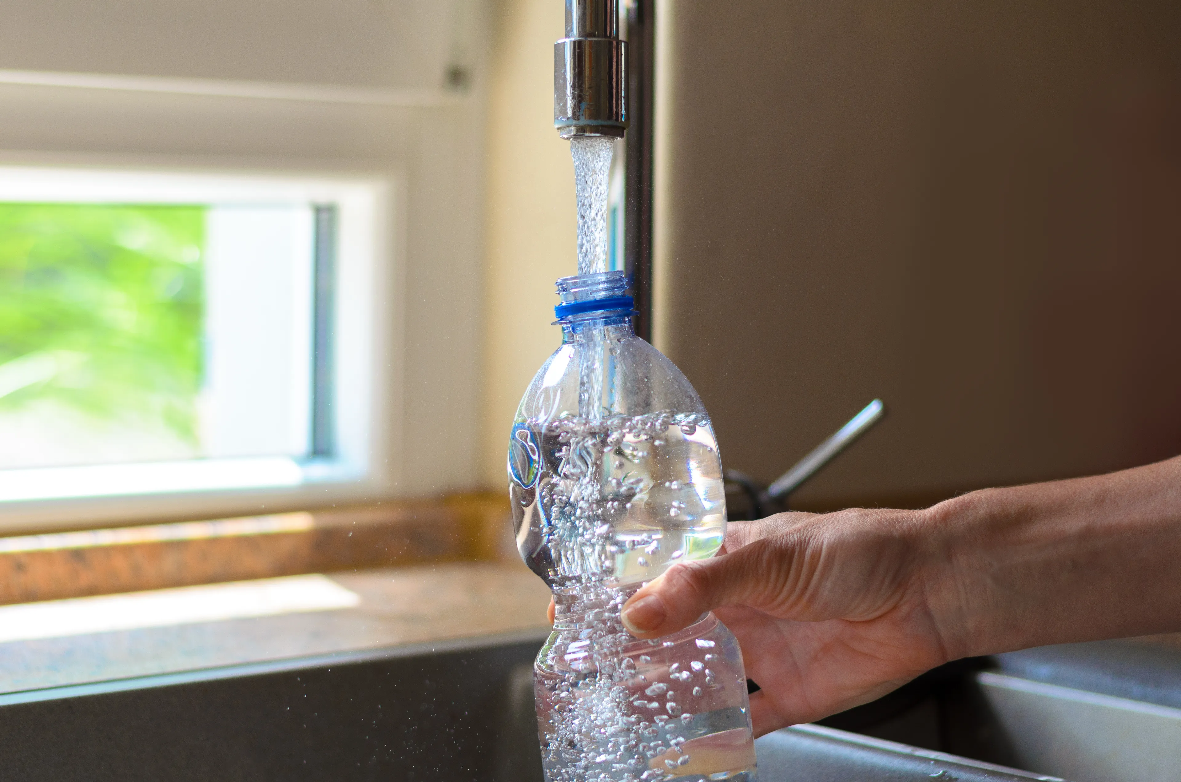 Plastikflasche wird in der Küche mit Trinkwasser aus dem Hahn befüllt