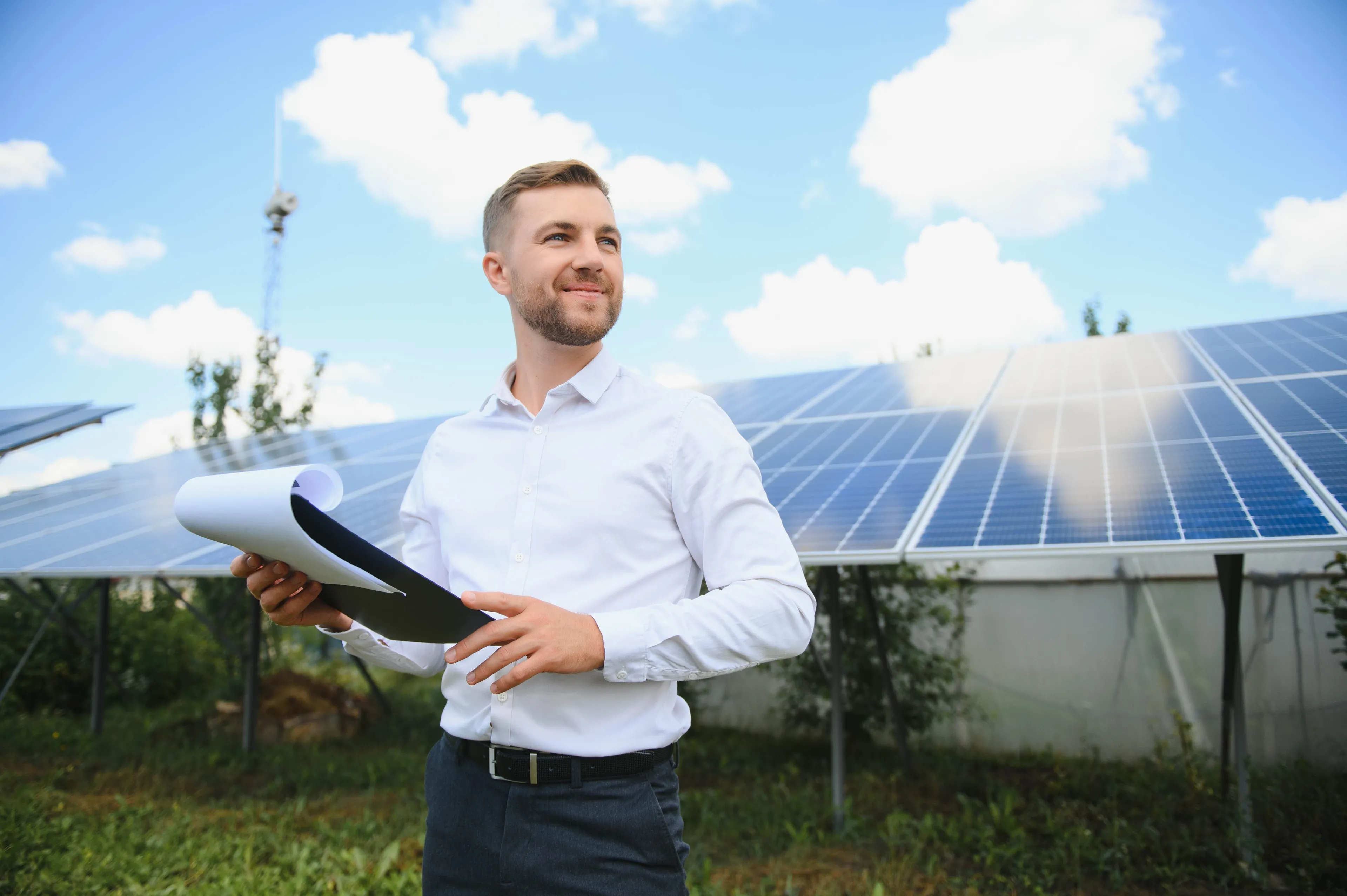 Ein Mann mit Unterlagen steht vor einer Photovoltaikanlage und blickt optimistisch in die Ferne