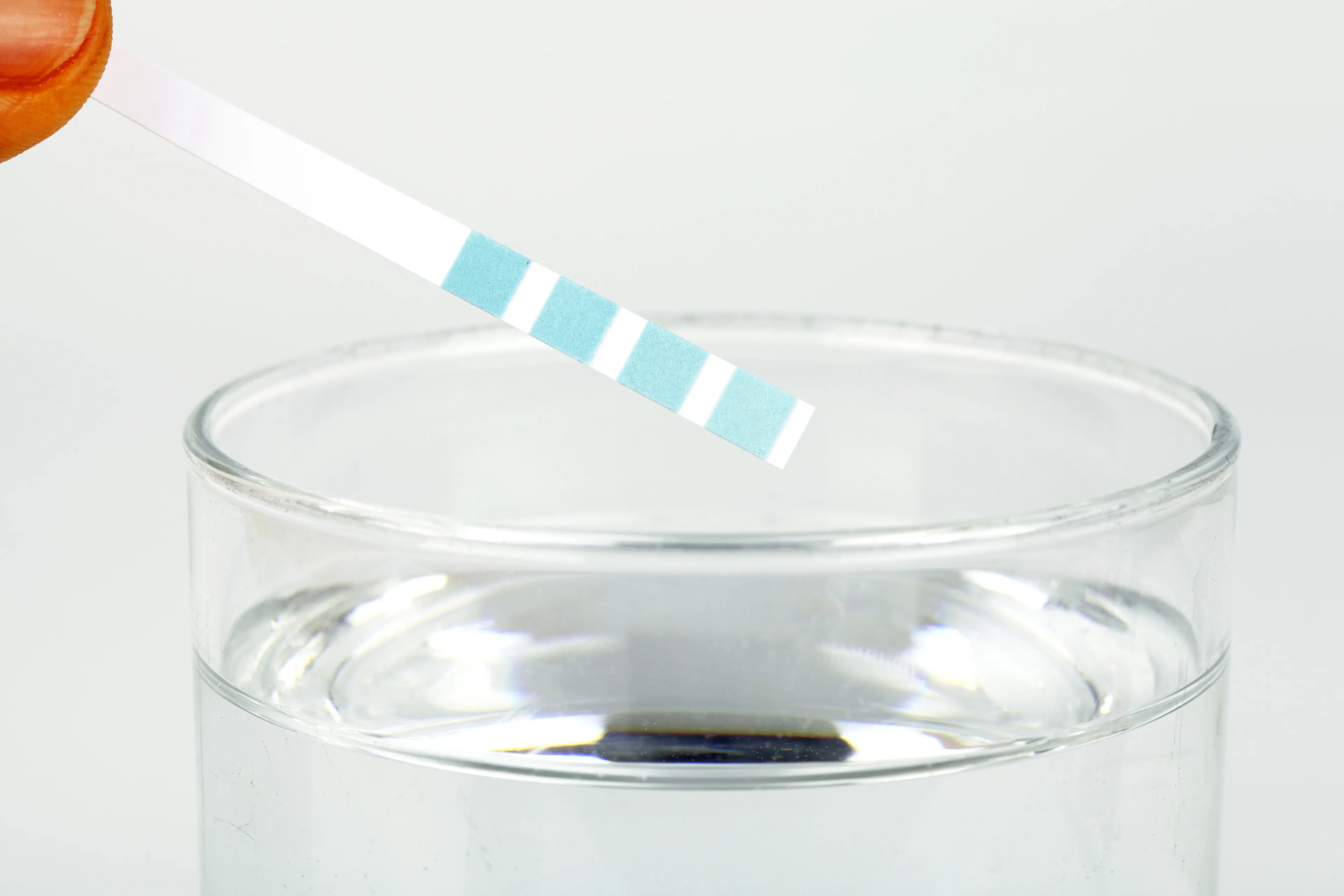 Wasserhärte-teststreifen wird über ein Glas mit Wasser gehalten.