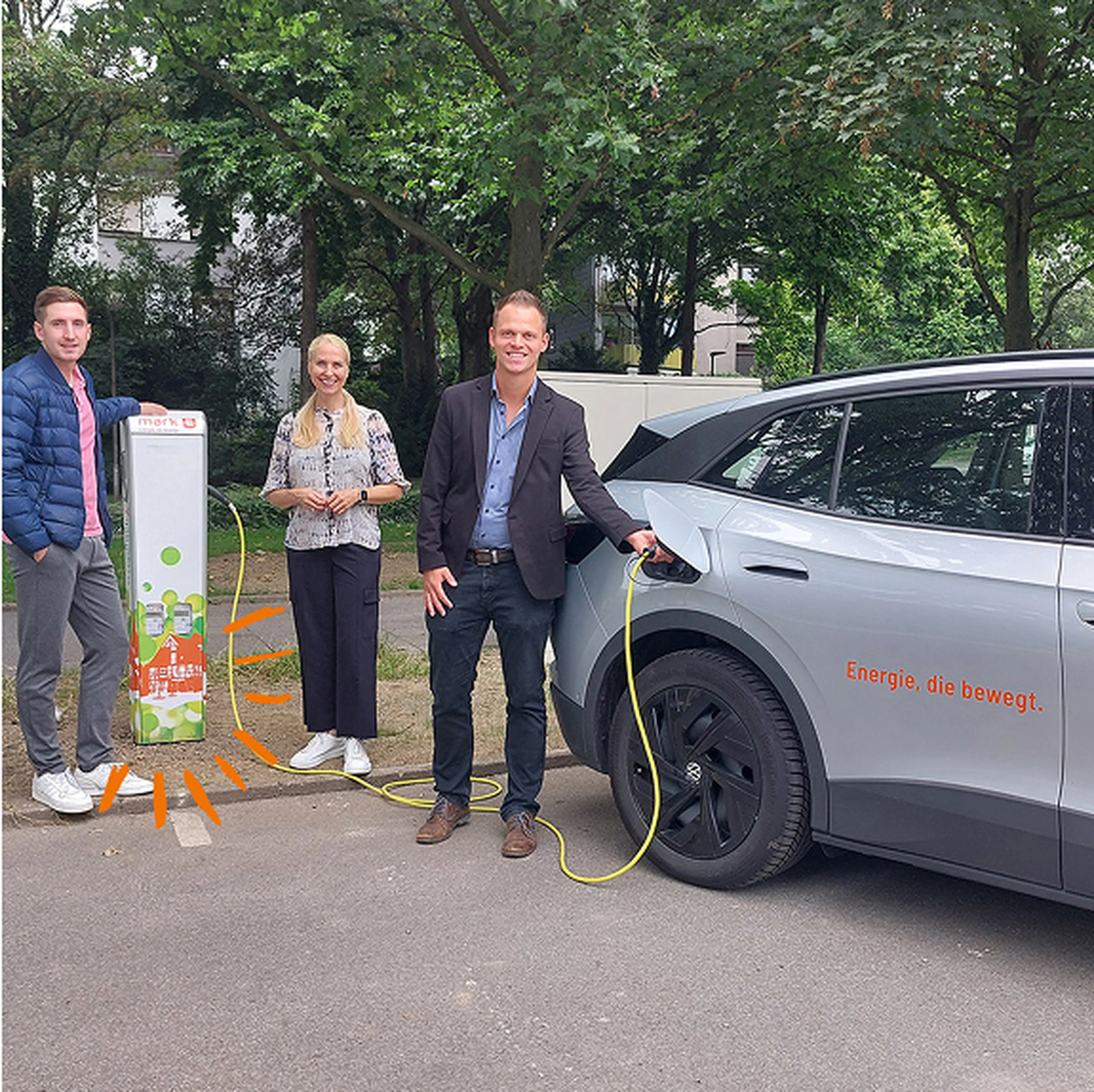 Drei Personen schauen in die Kamera - Auto wird von einem Mann an der Ladesäule geladen