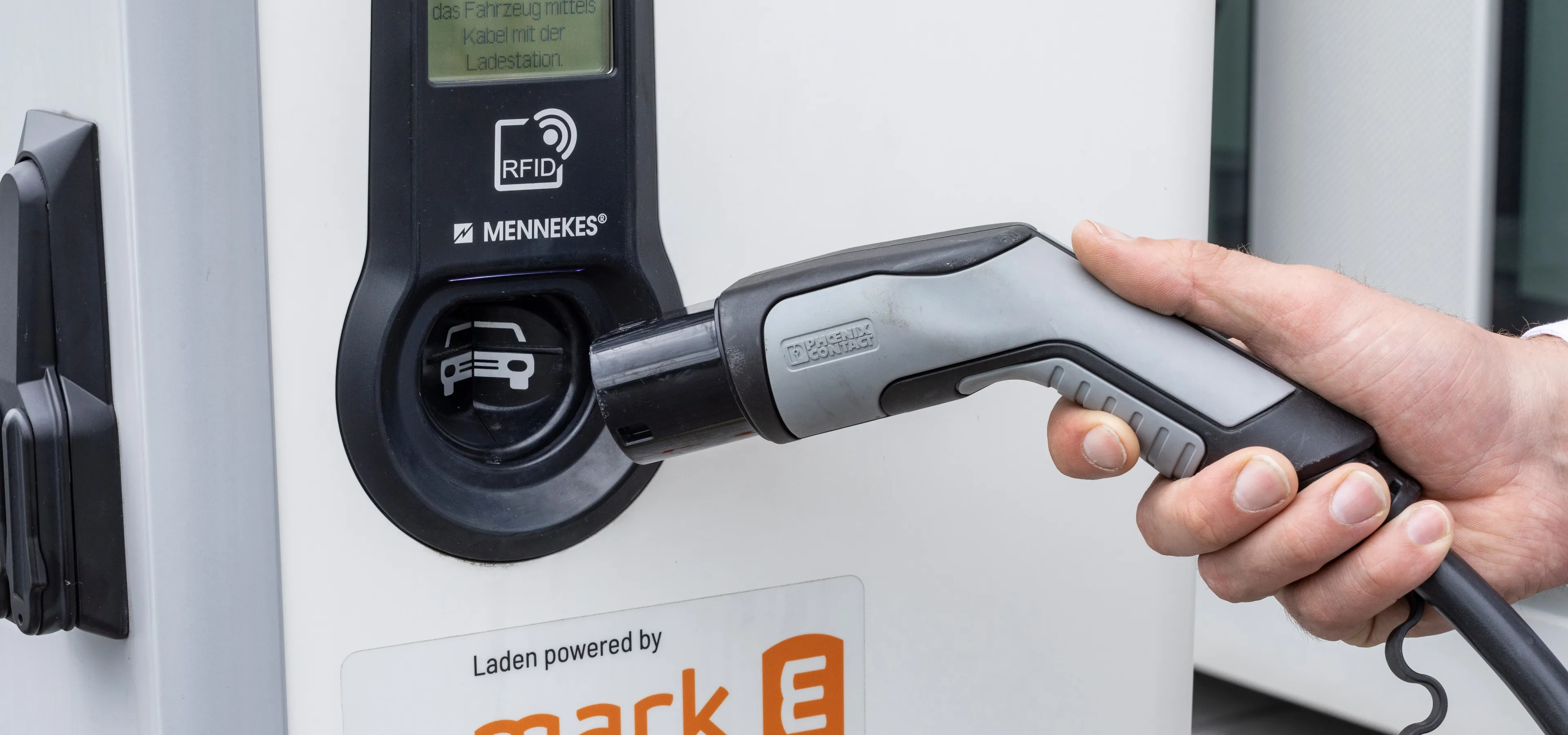 Hand steckt ein Ladekabel in eine Ladesäule für Elektrofahrzeuge.