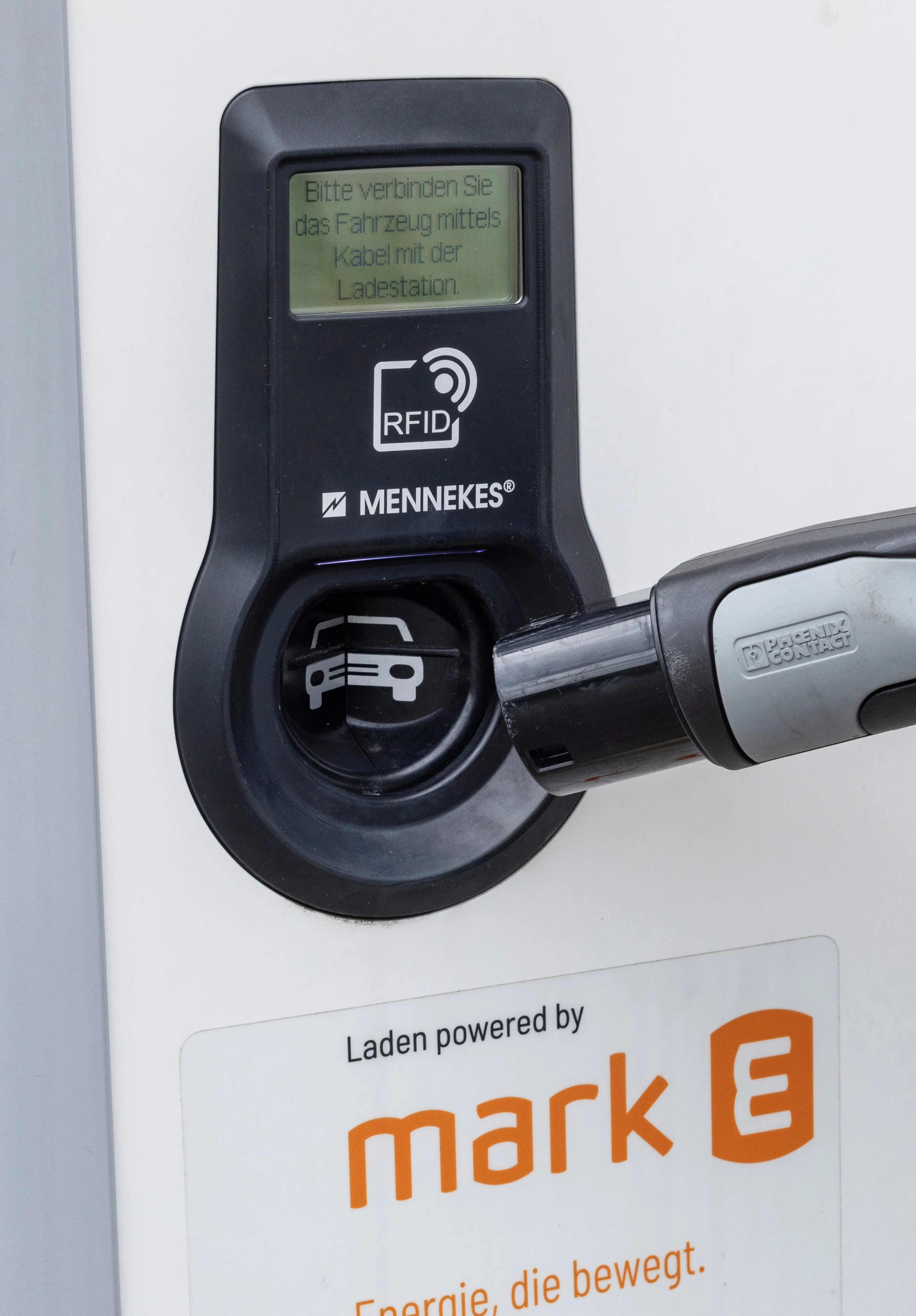 Hand steckt ein Ladekabel in eine Ladesäule für Elektrofahrzeuge.