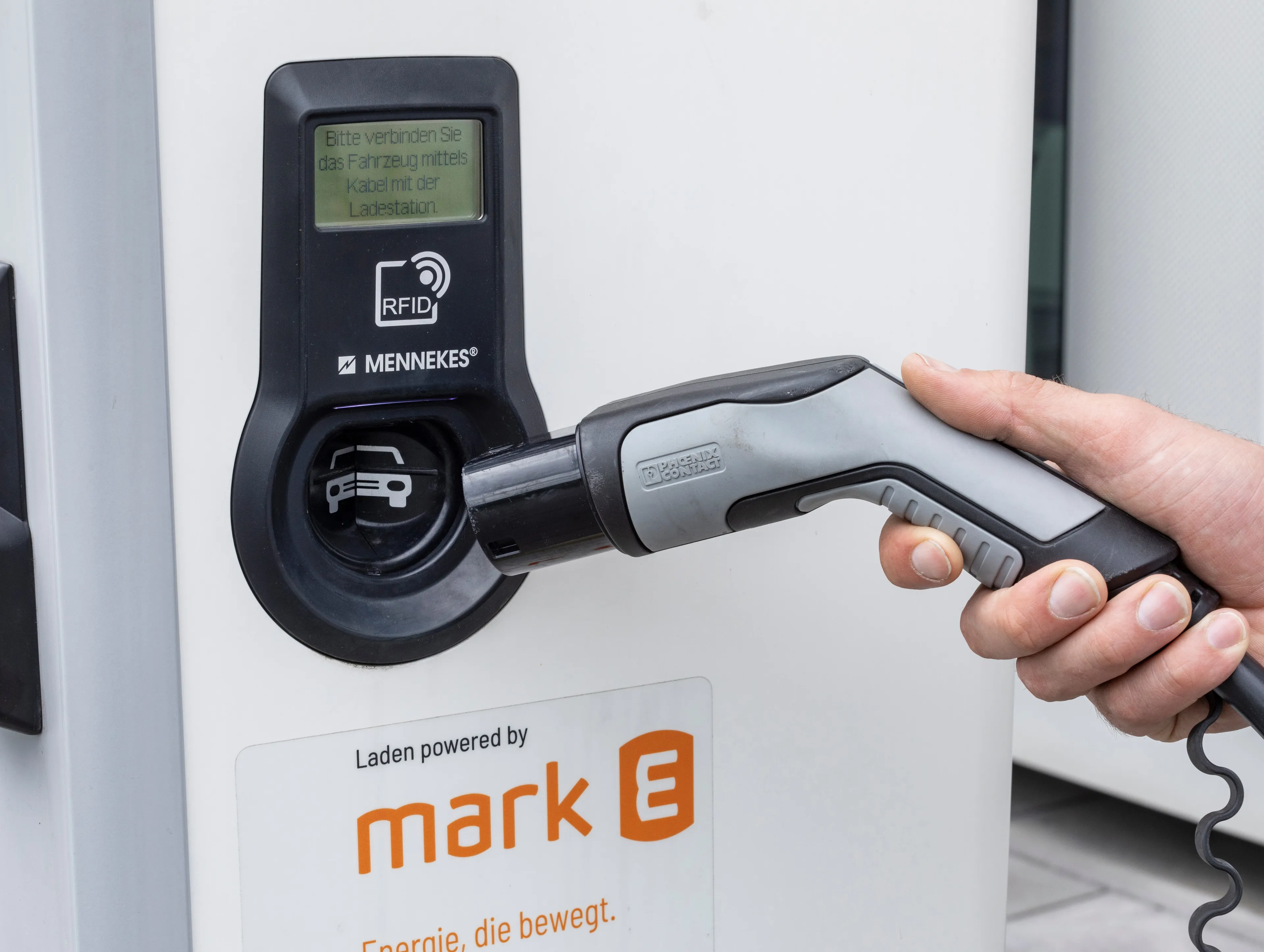 Hand steckt ein Ladekabel in eine Ladesäule für Elektrofahrzeuge.