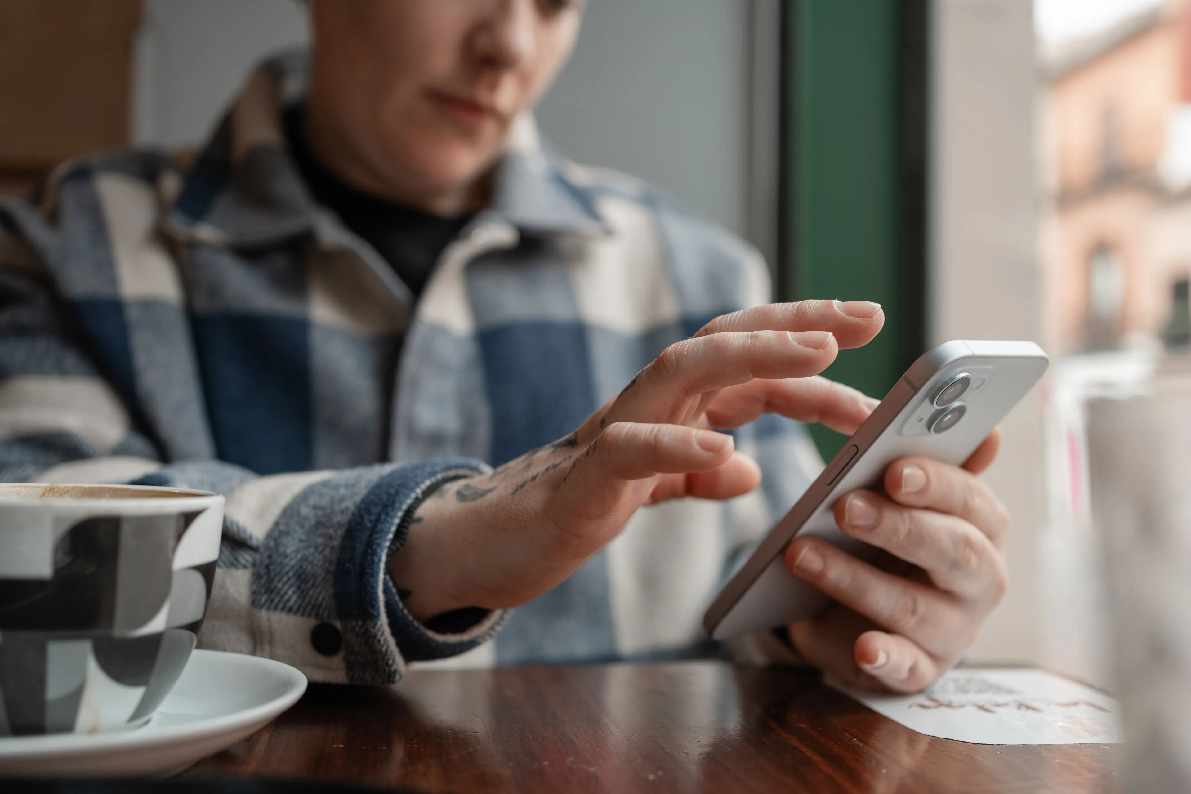 Person sitzt in einem Café und tippt auf dem Smartphone