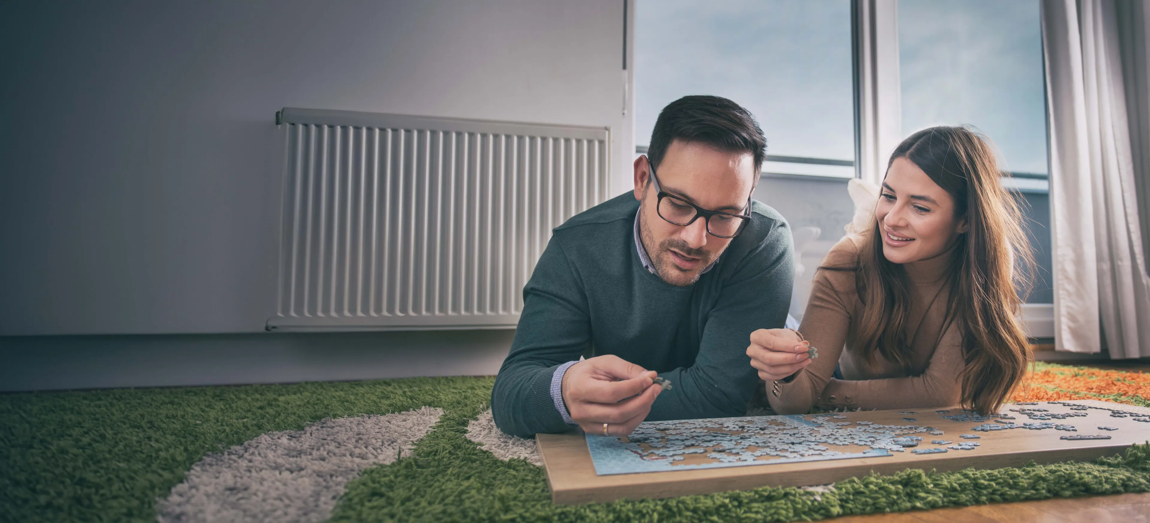 Paar puzzelt gemeinsam vor dem Heizkörper und genießt die angenehme Wohnwärme