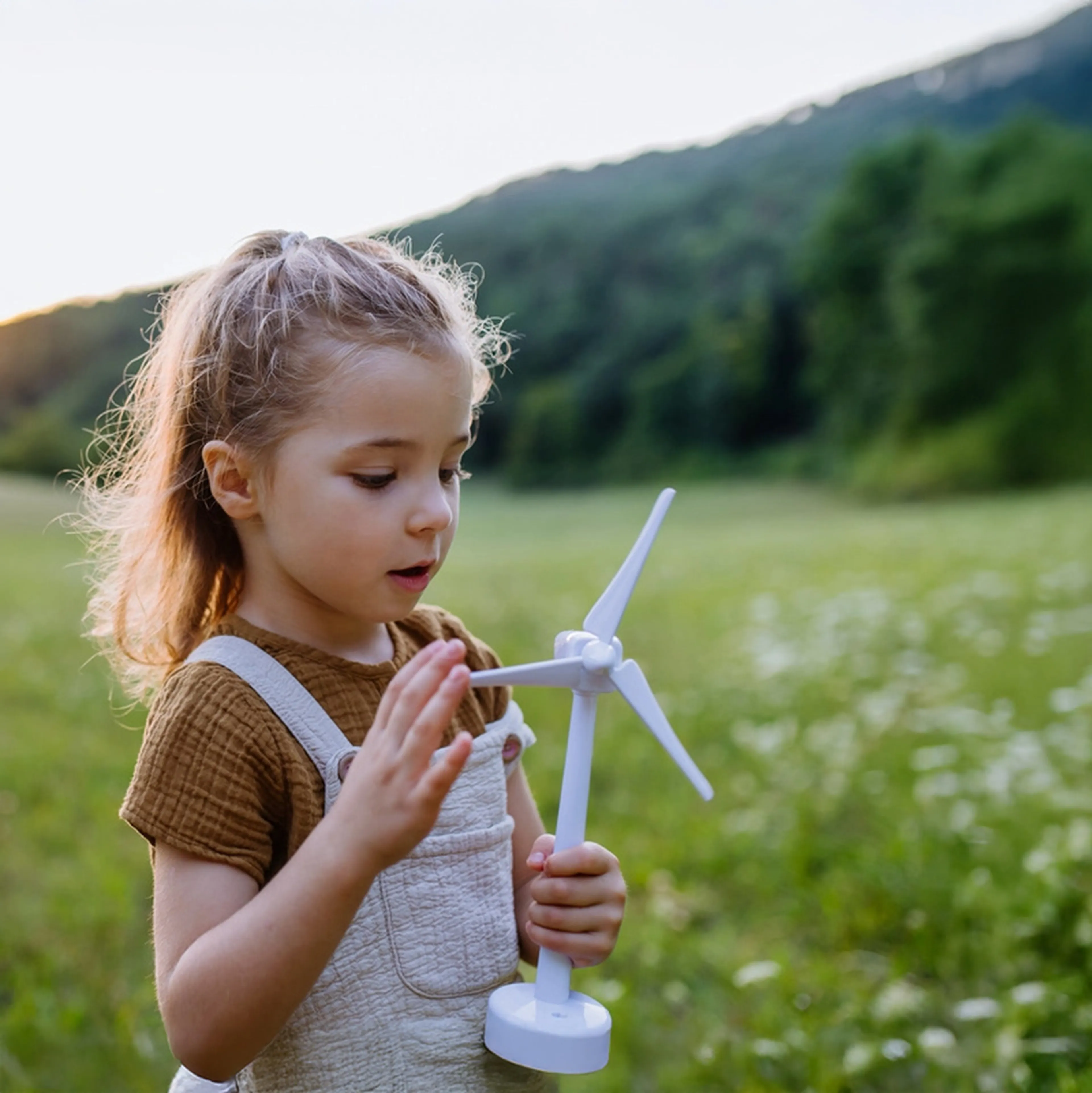 Kleines Mädchen steht auf einer Wiese mit einem Windkraftrad in der Hand